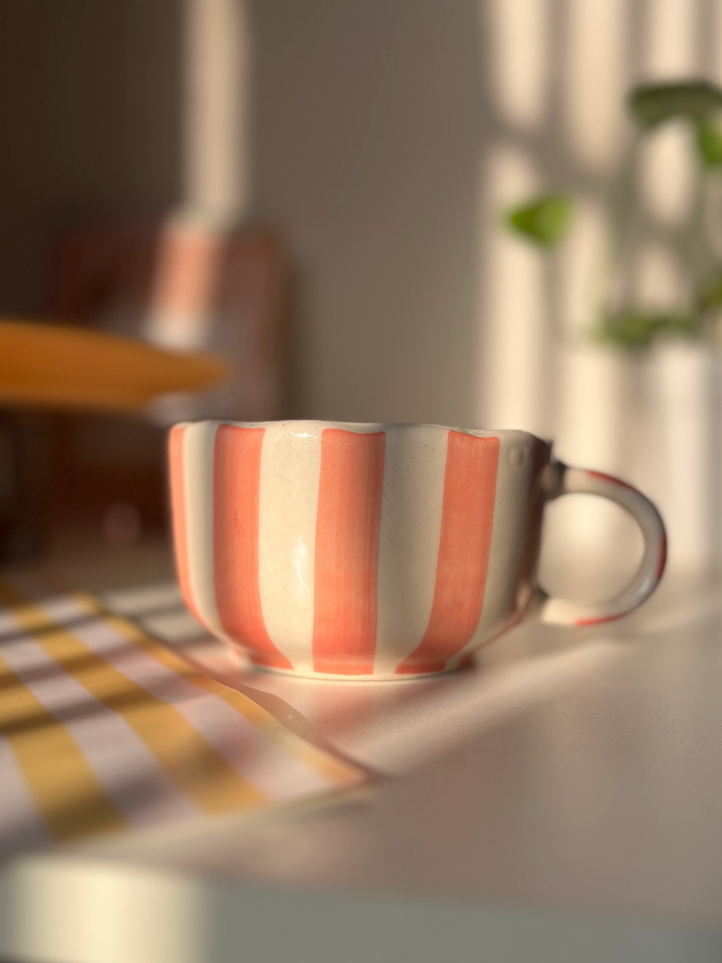 Striped peach ceramic cup on a table with a blurred background