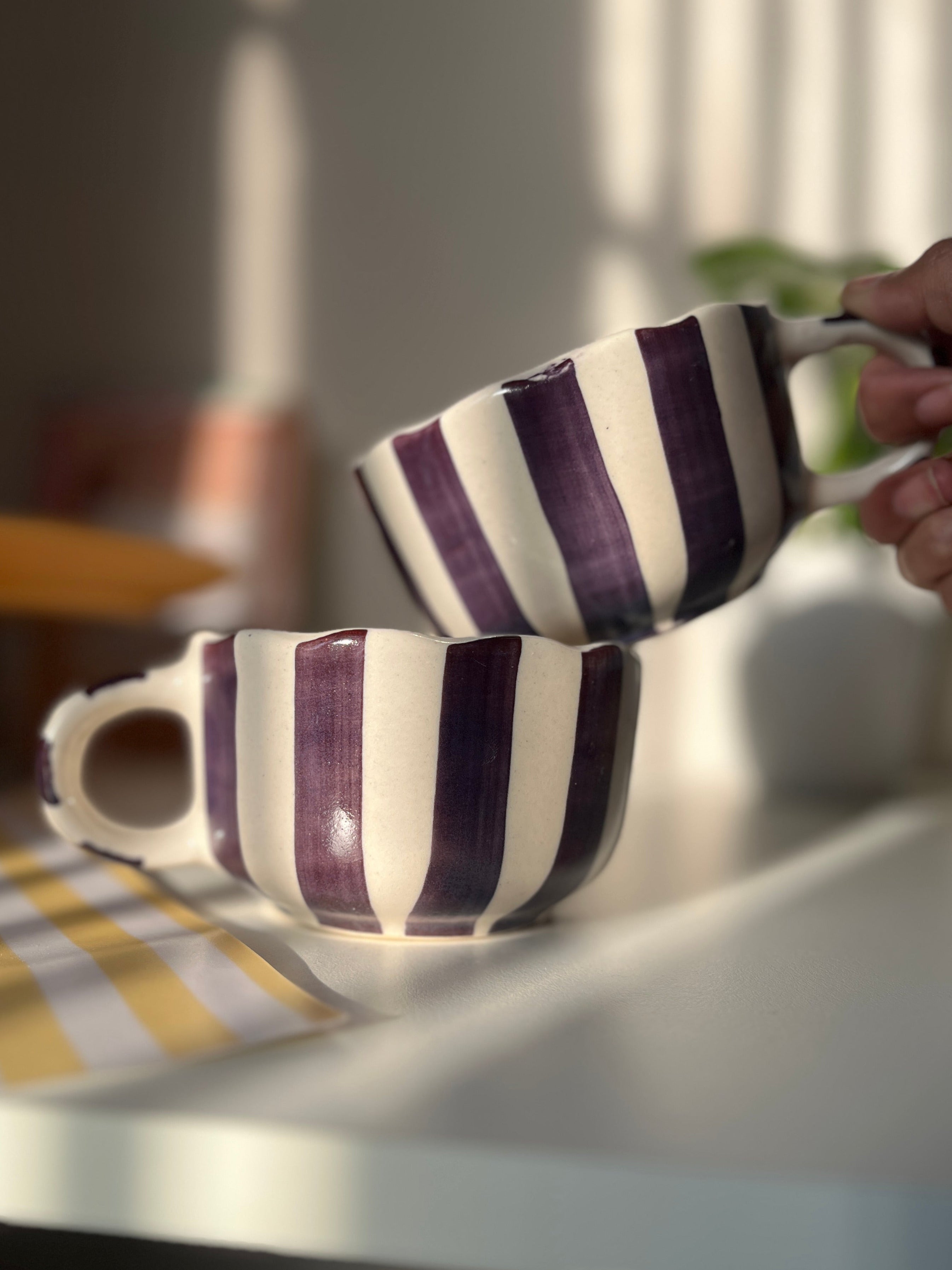 Two striped purple and white mugs on a table with a blurred background