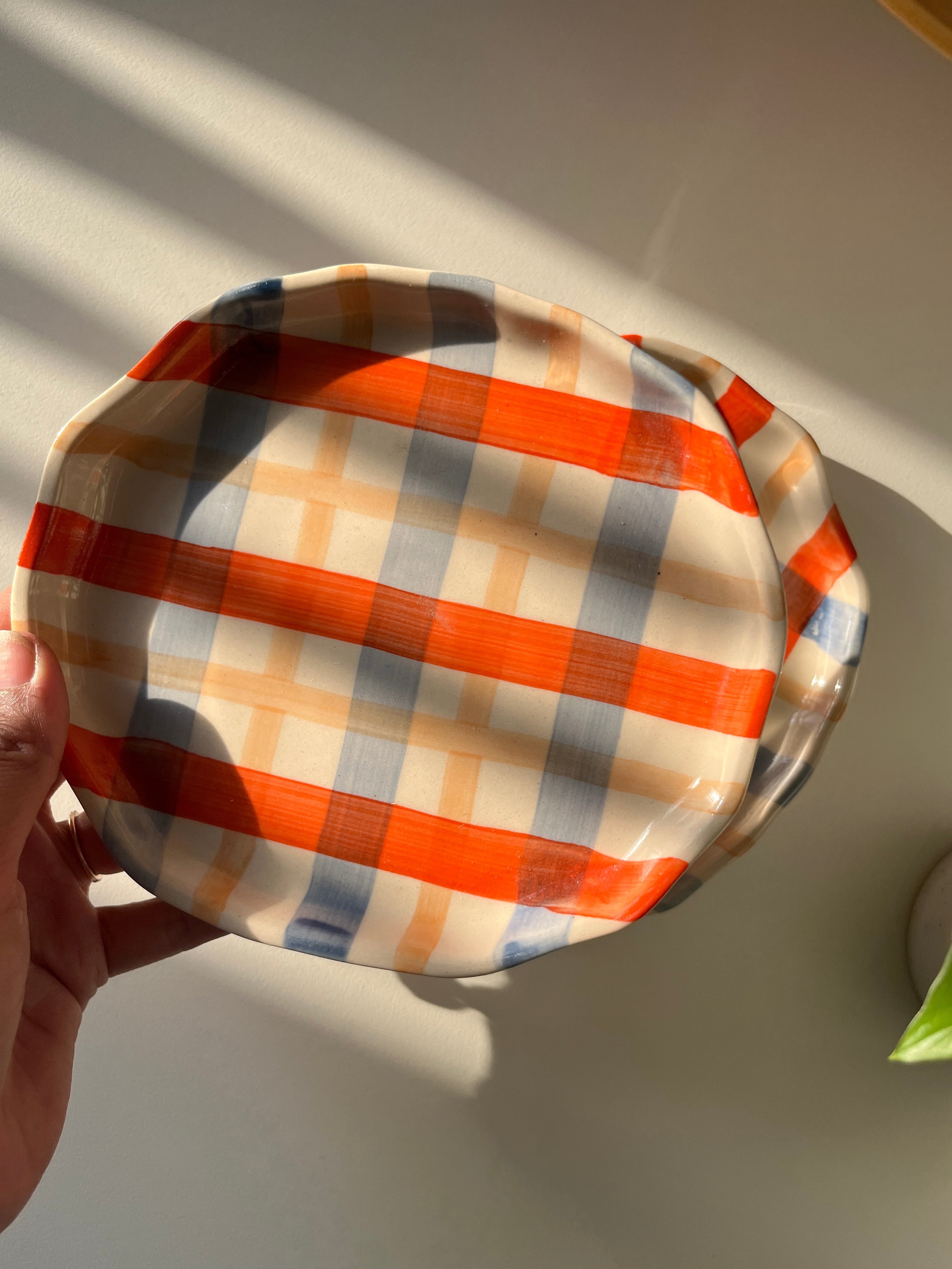 Round, checkered fabric styled plate held by a hand on a light background