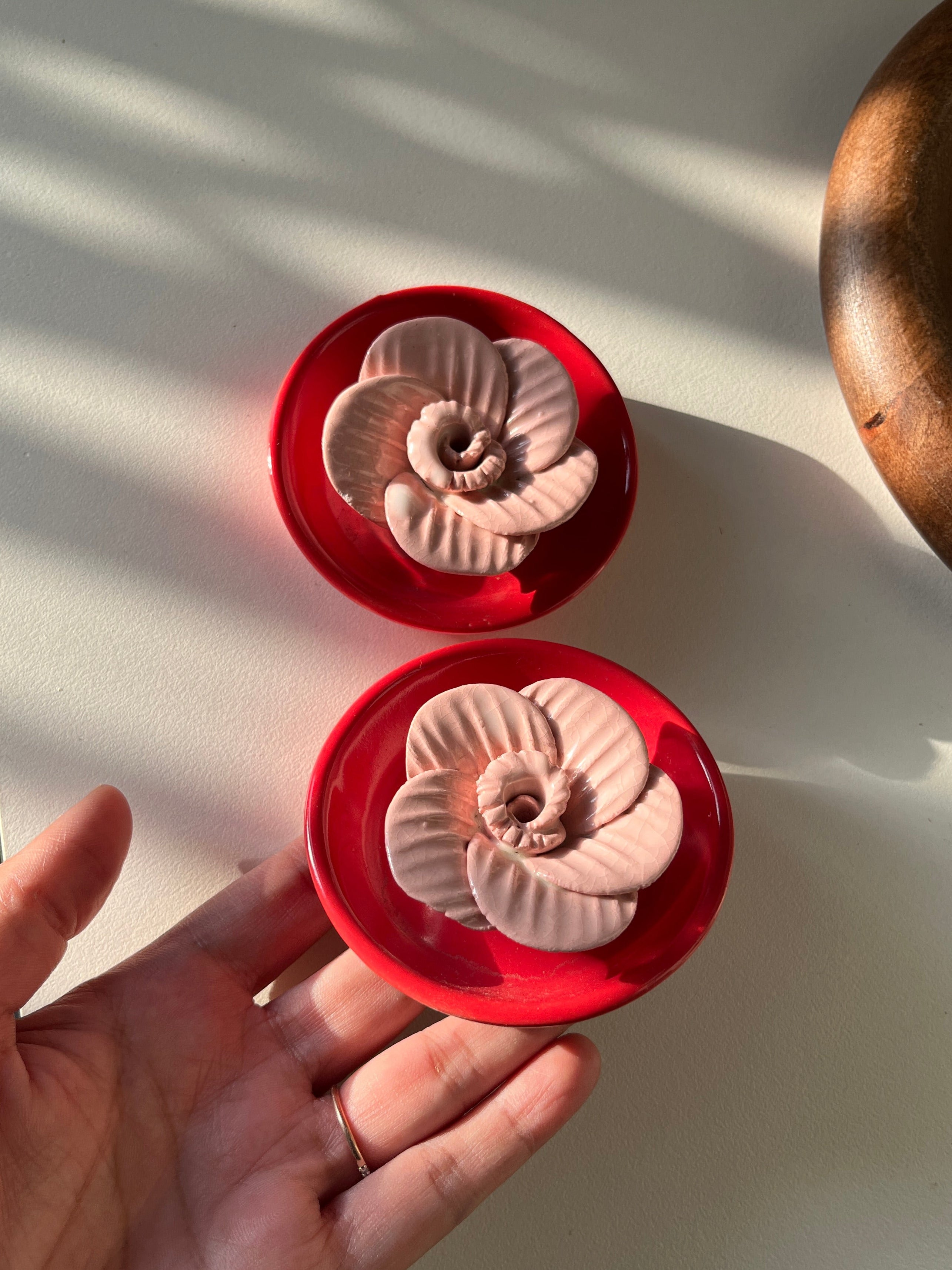 Two red containers with shell-like designs on a white surface, one of which is held by a hand.