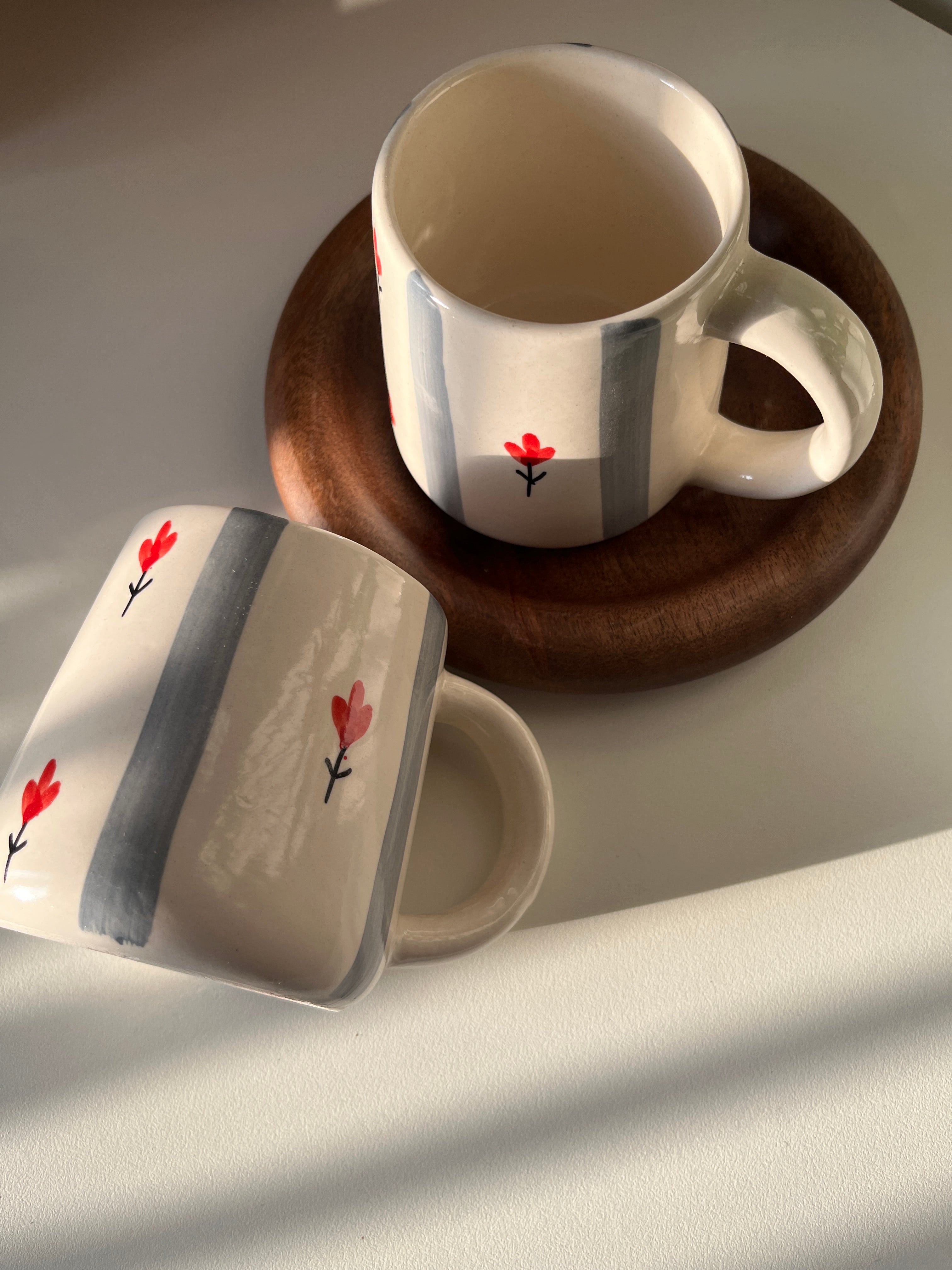 Two ceramic mugs with floral designs on a wooden coaster.