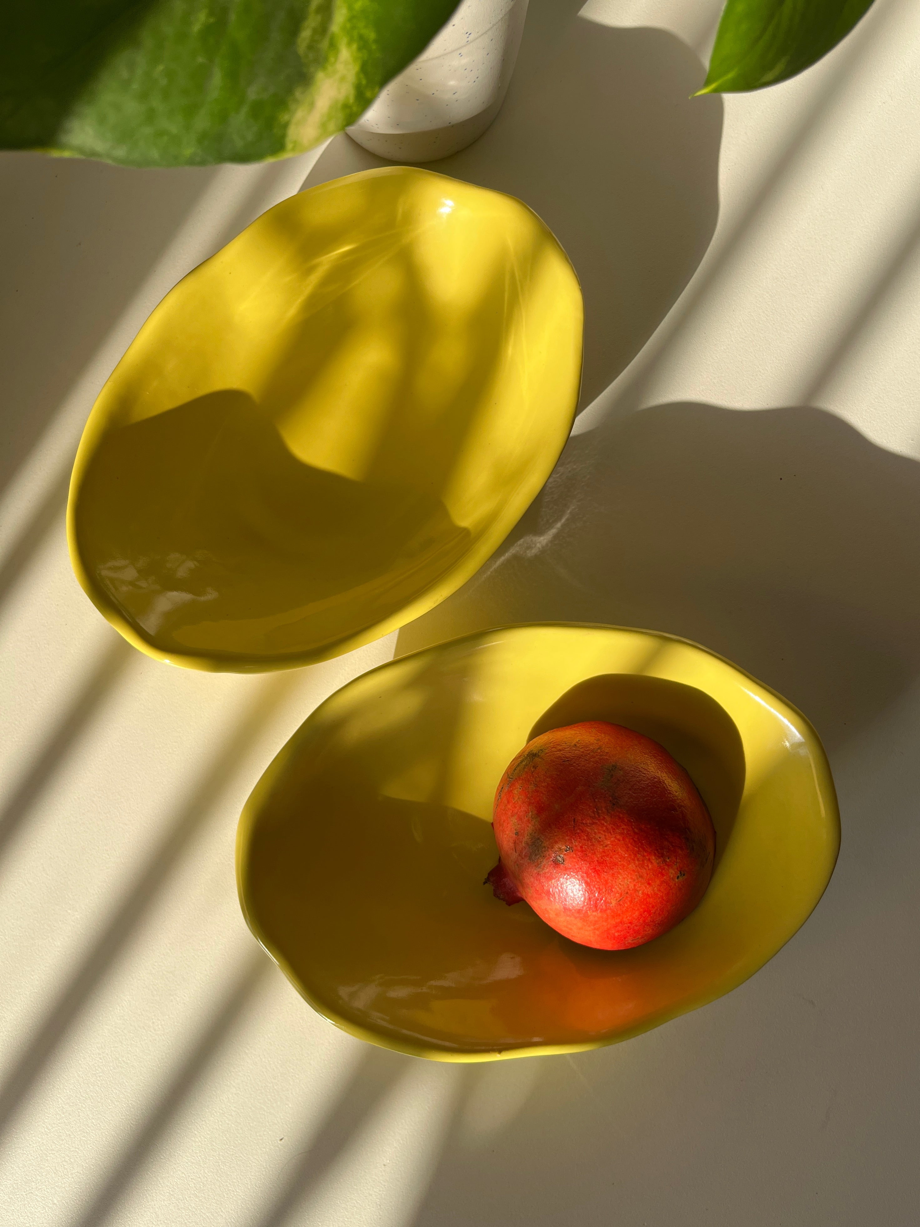 Two yellow ceramic bowls with a pomegranate on a light background