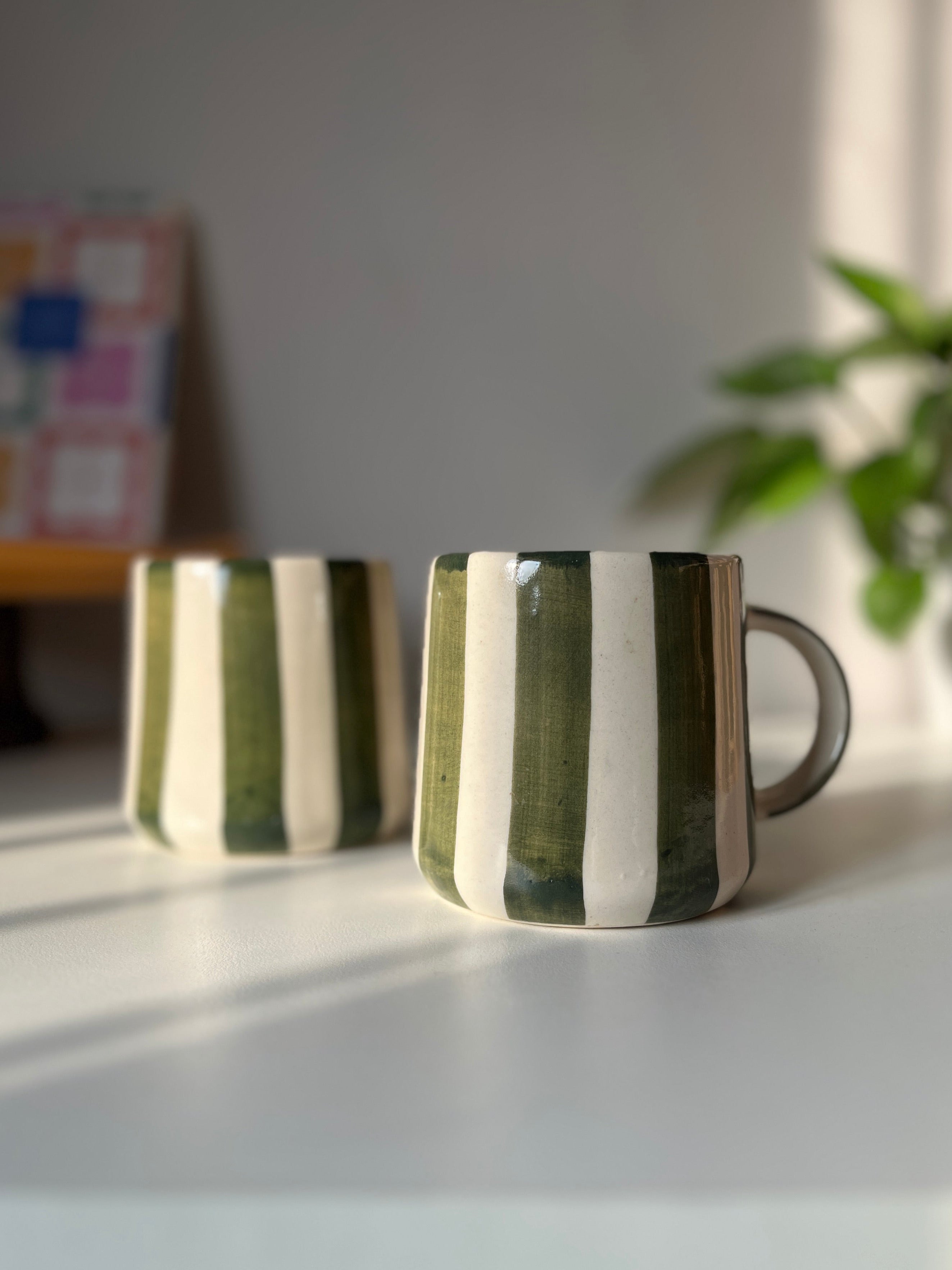 Two green ceramic coffee mugs with striped design on a light surface