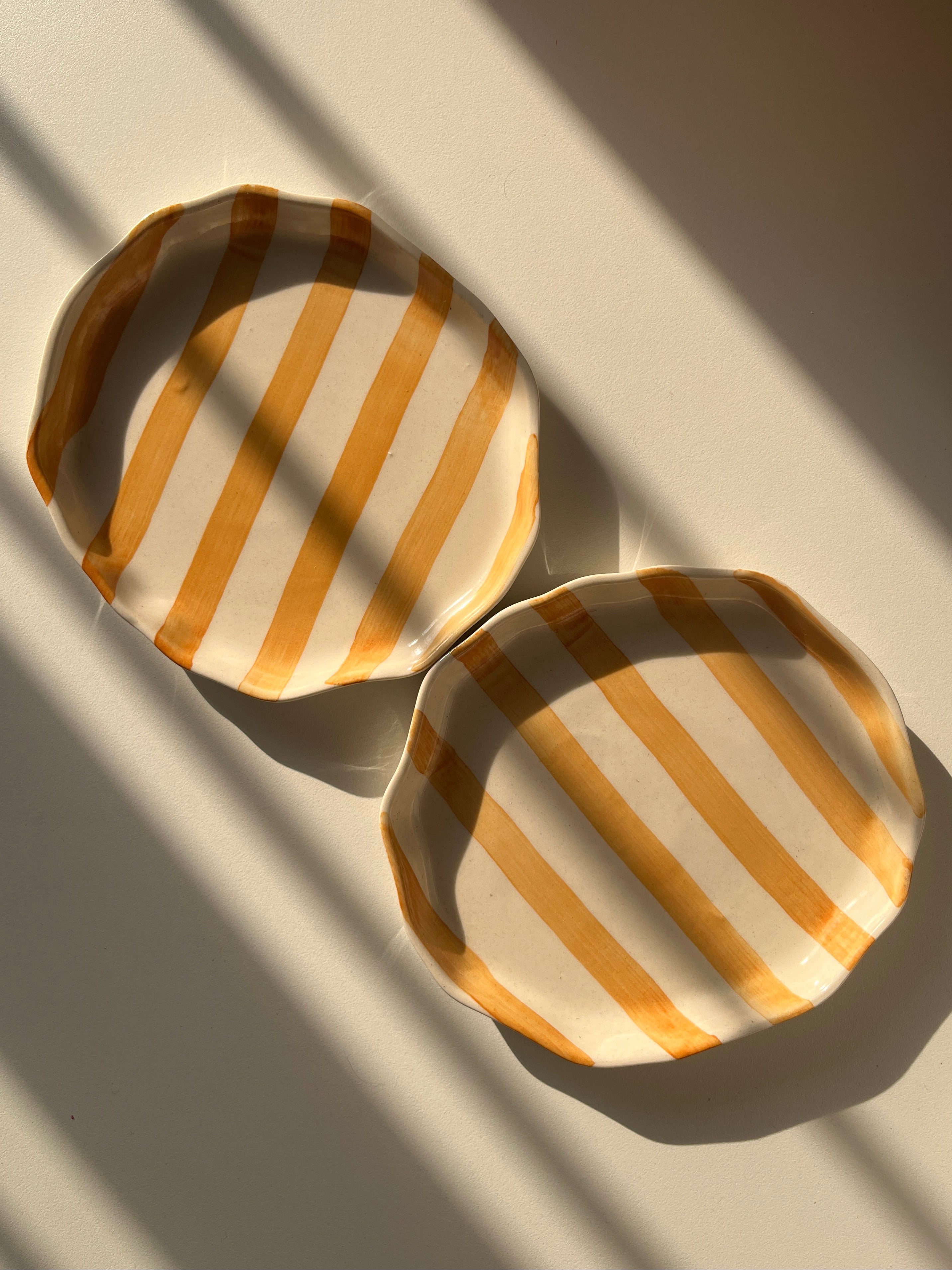 Two round, striped coaster plates on a textured surface with shadows.
