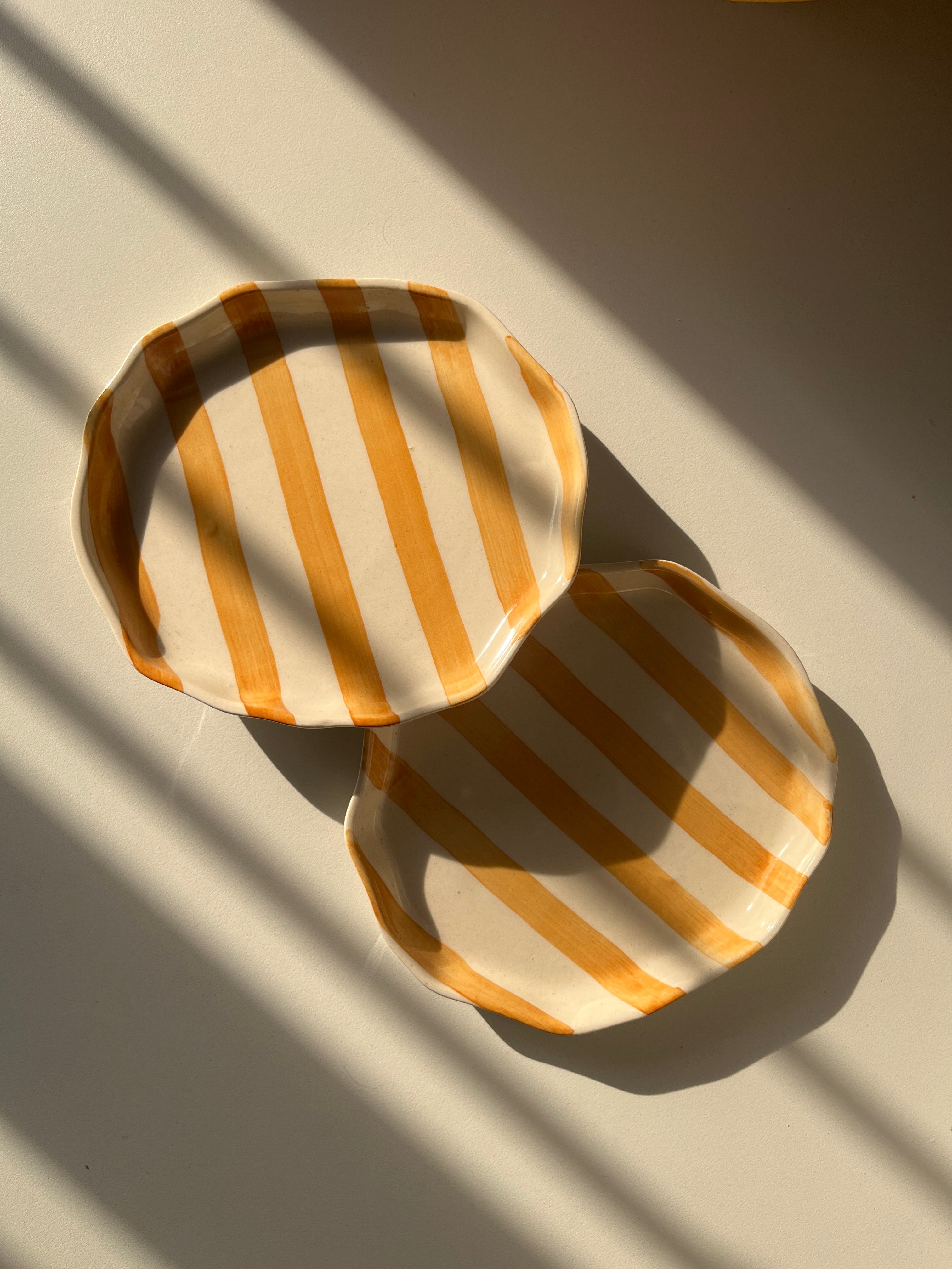 Two round, striped plates on a textured surface with shadows.