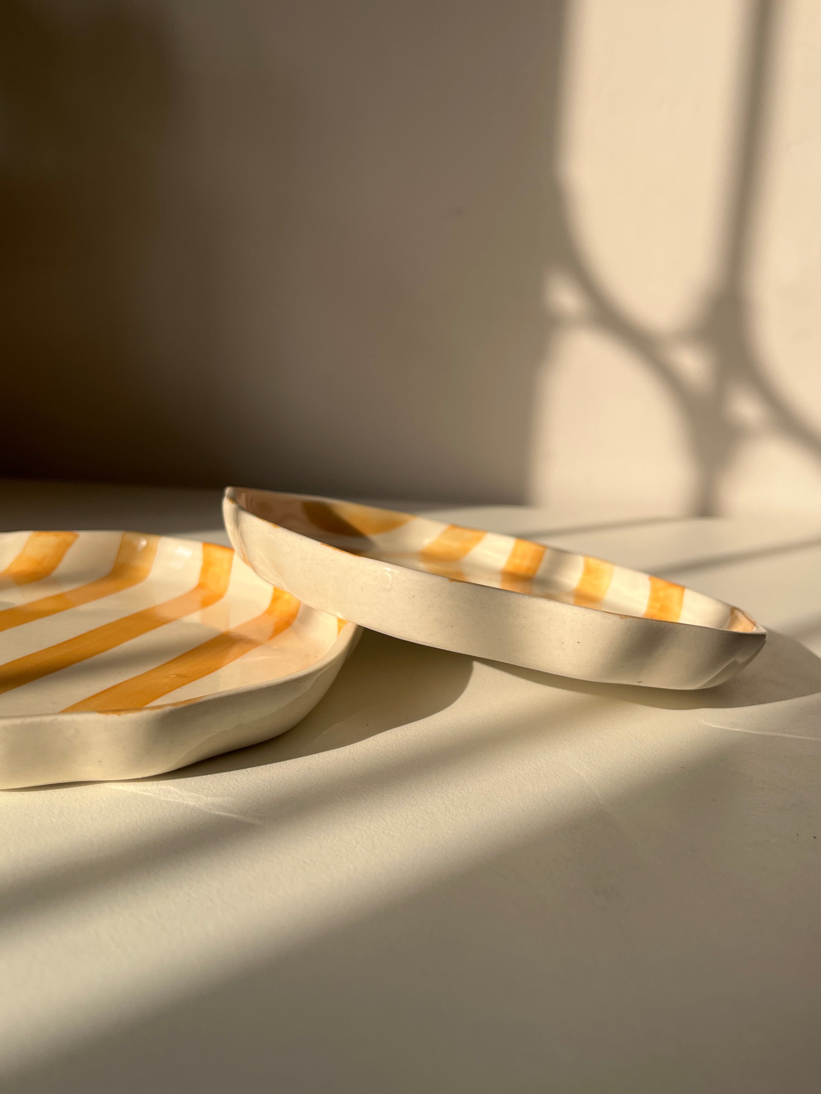 Modern striped plates with a shadow on a neutral wall and white table