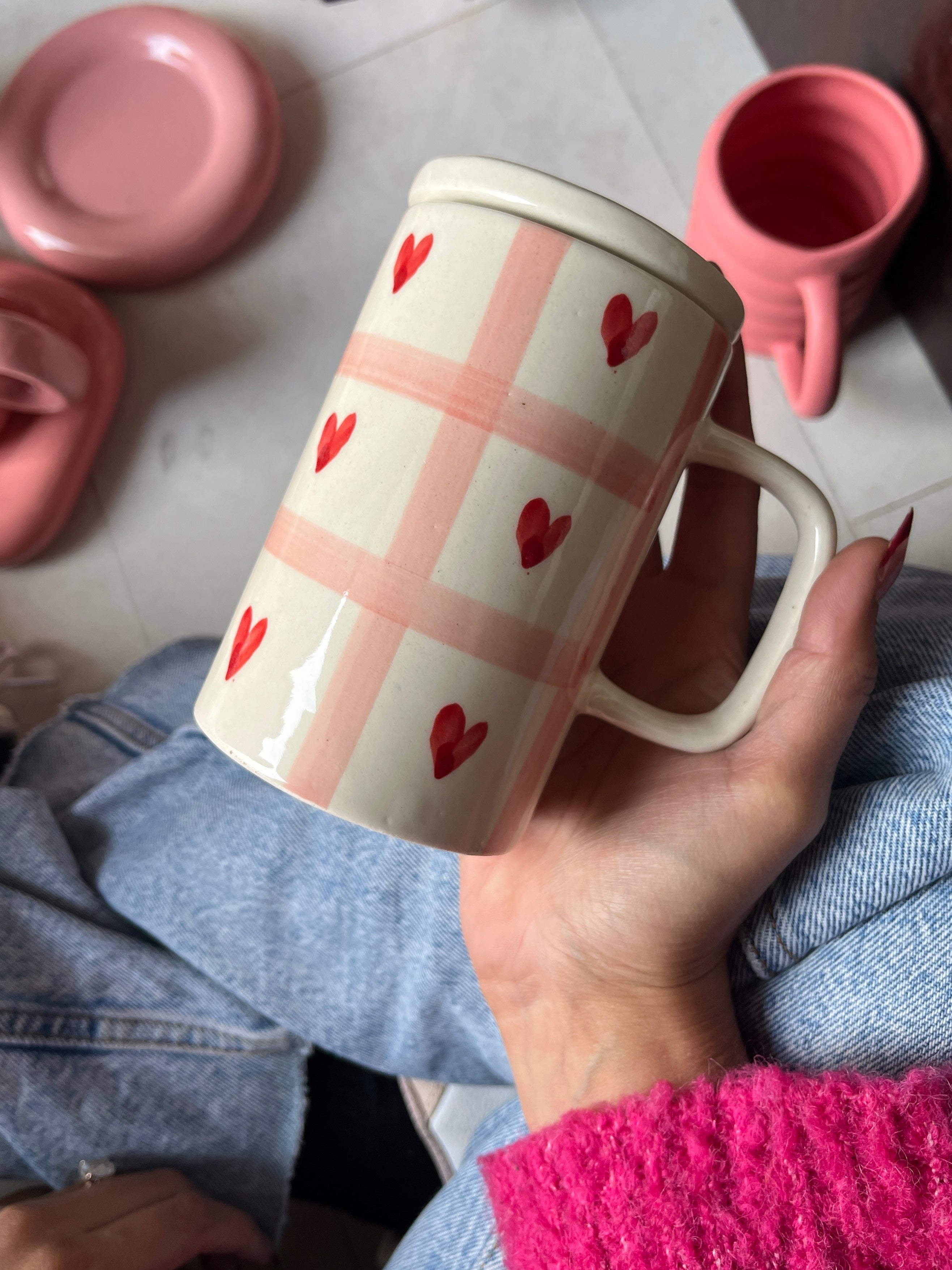 Hand holding a mug with red heart pattern on a checkered background