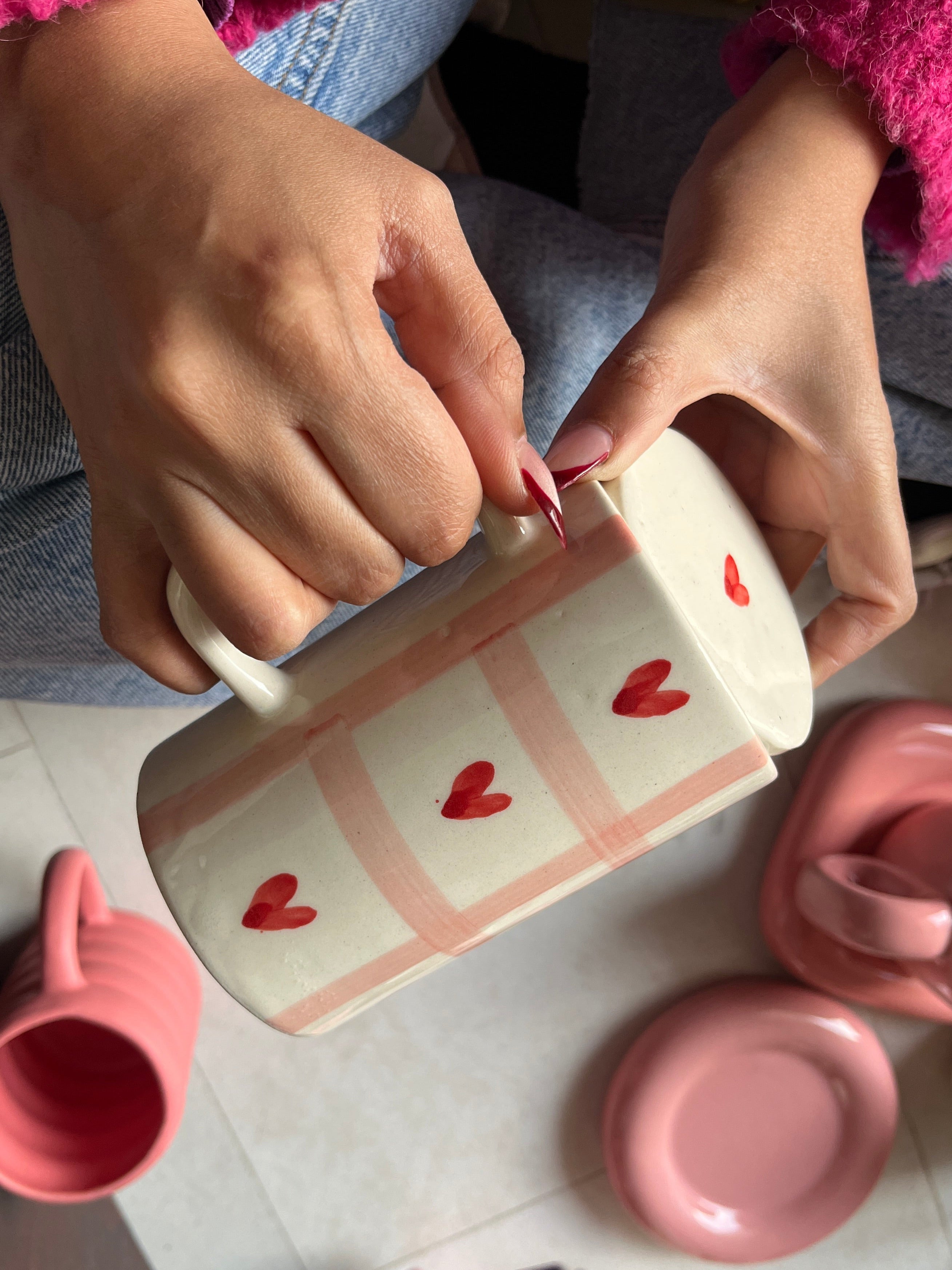 Person holding a pink mug with heart designs on a tiled floor.
