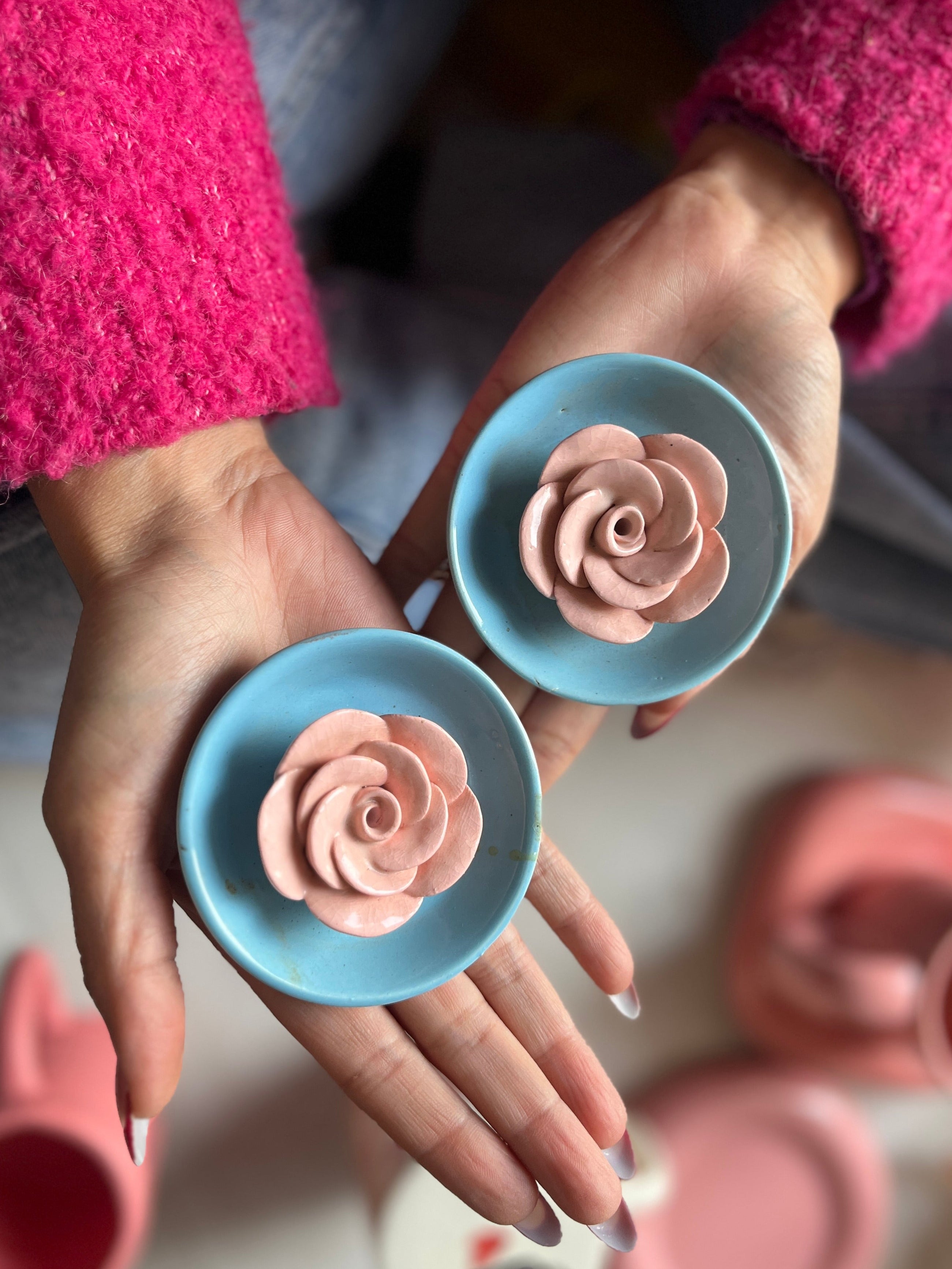 Hands holding blue incense stick holders with pink rose-shaped ceramic flower in 3D