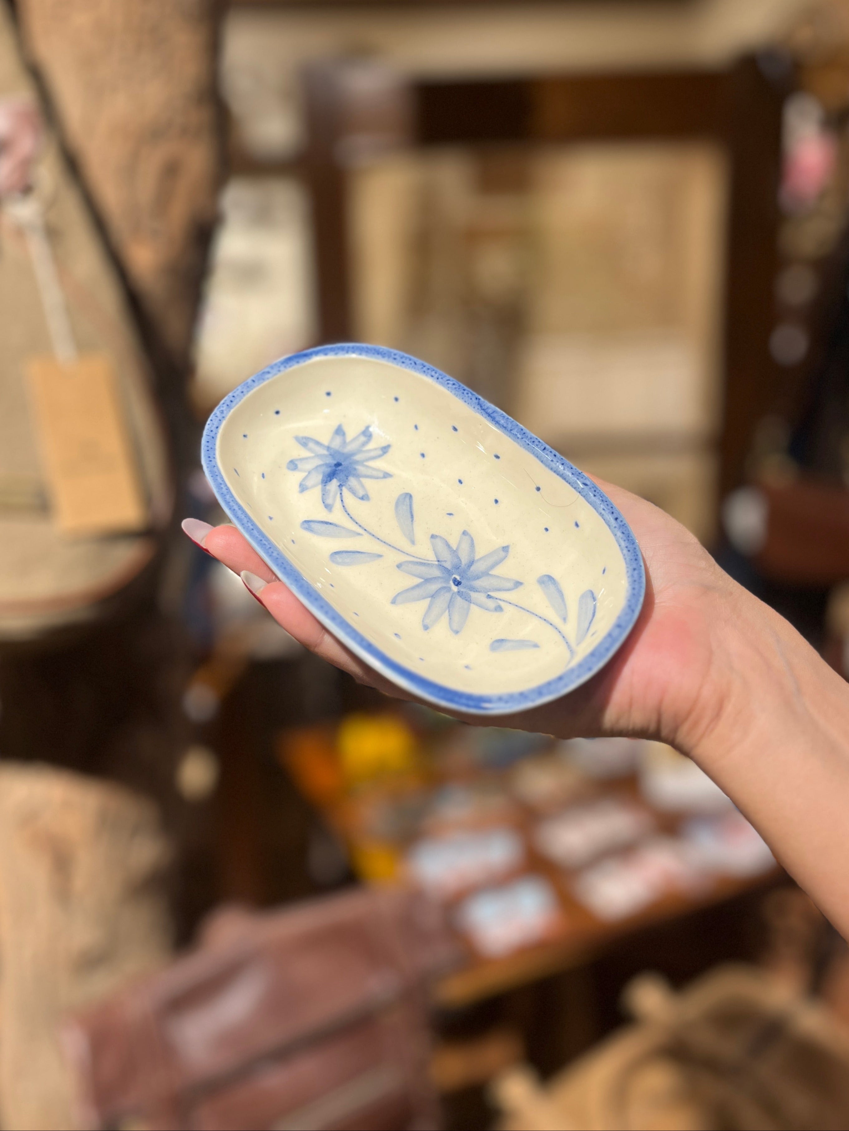 Hand holding a ceramic dish with blue floral patterns in a store setting