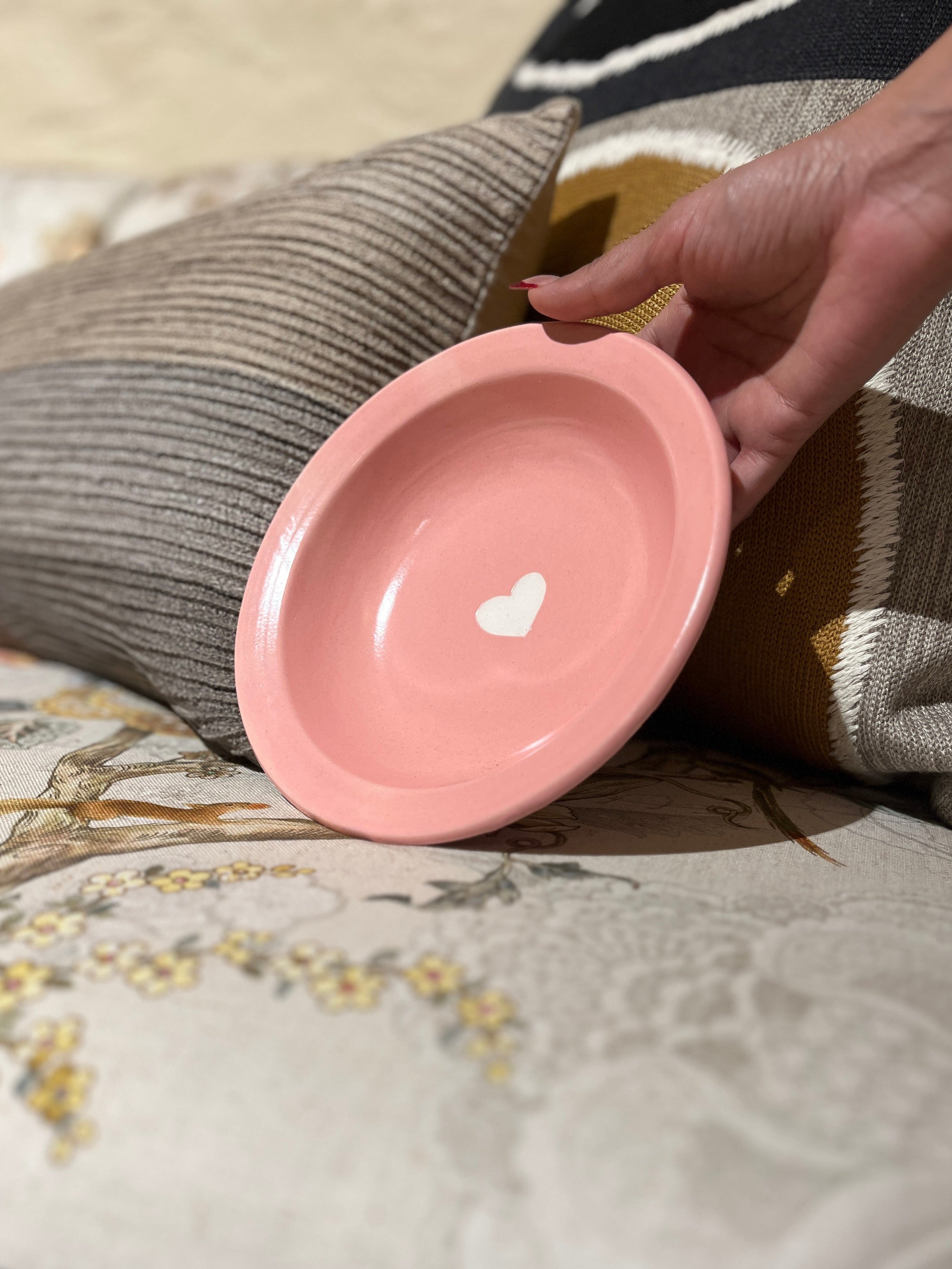 Hand holding a pink ceramic bowl with a heart design on a textured surface.