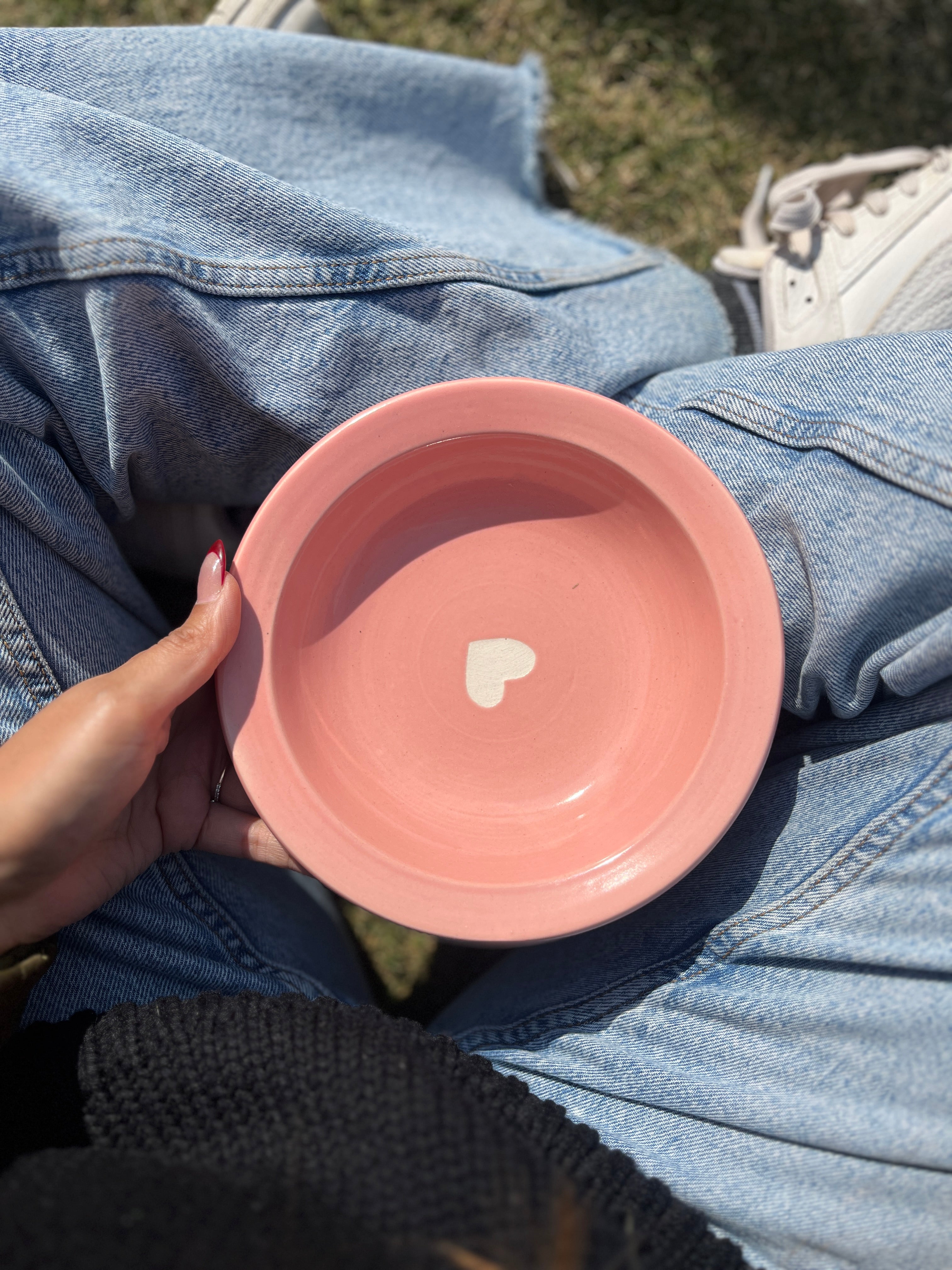 Pink ceramic bowl with a heart design held by a person wearing blue jeans.