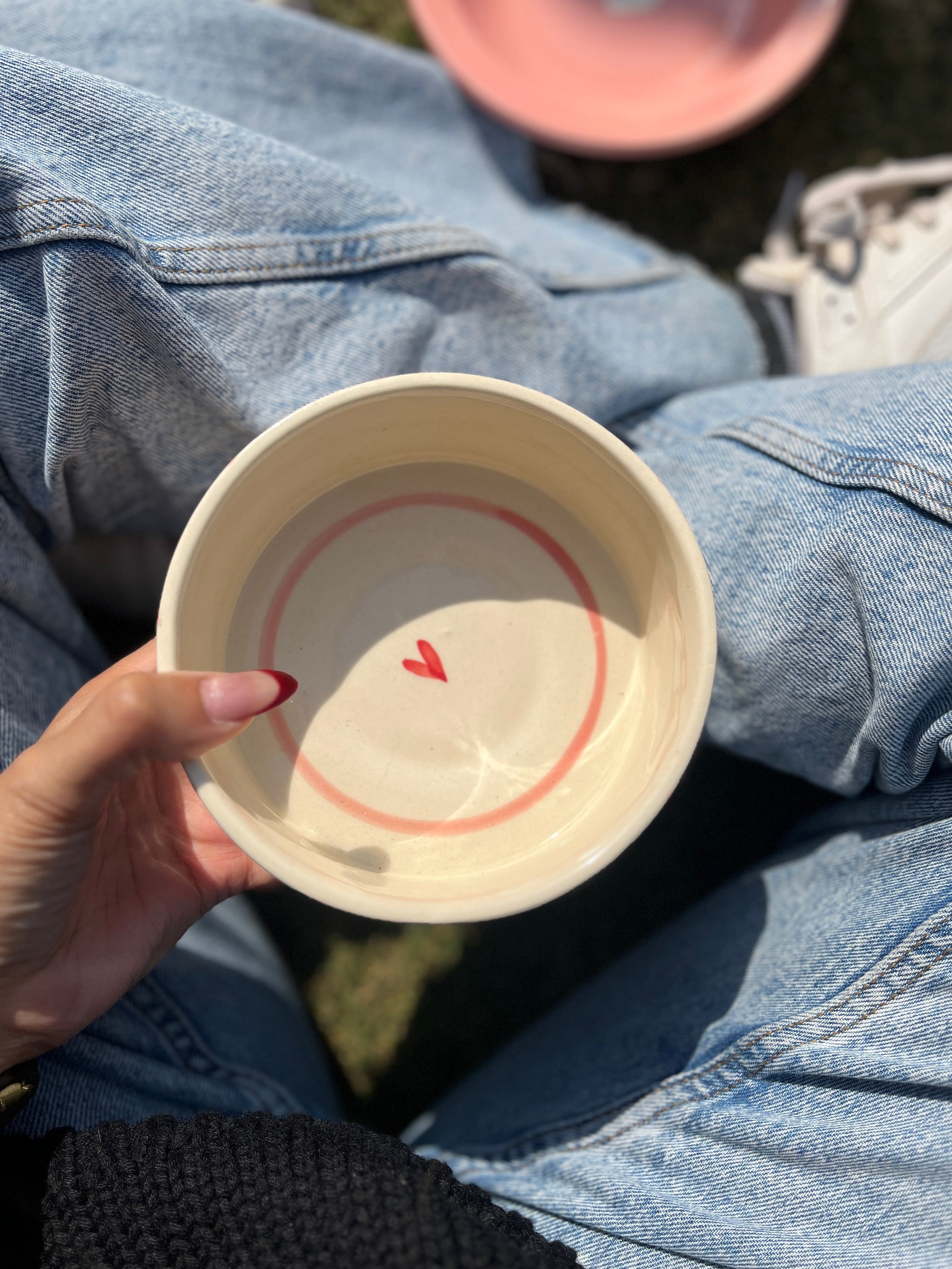 Hand holding a ceramic bowl with a red heart design on denim jeans.