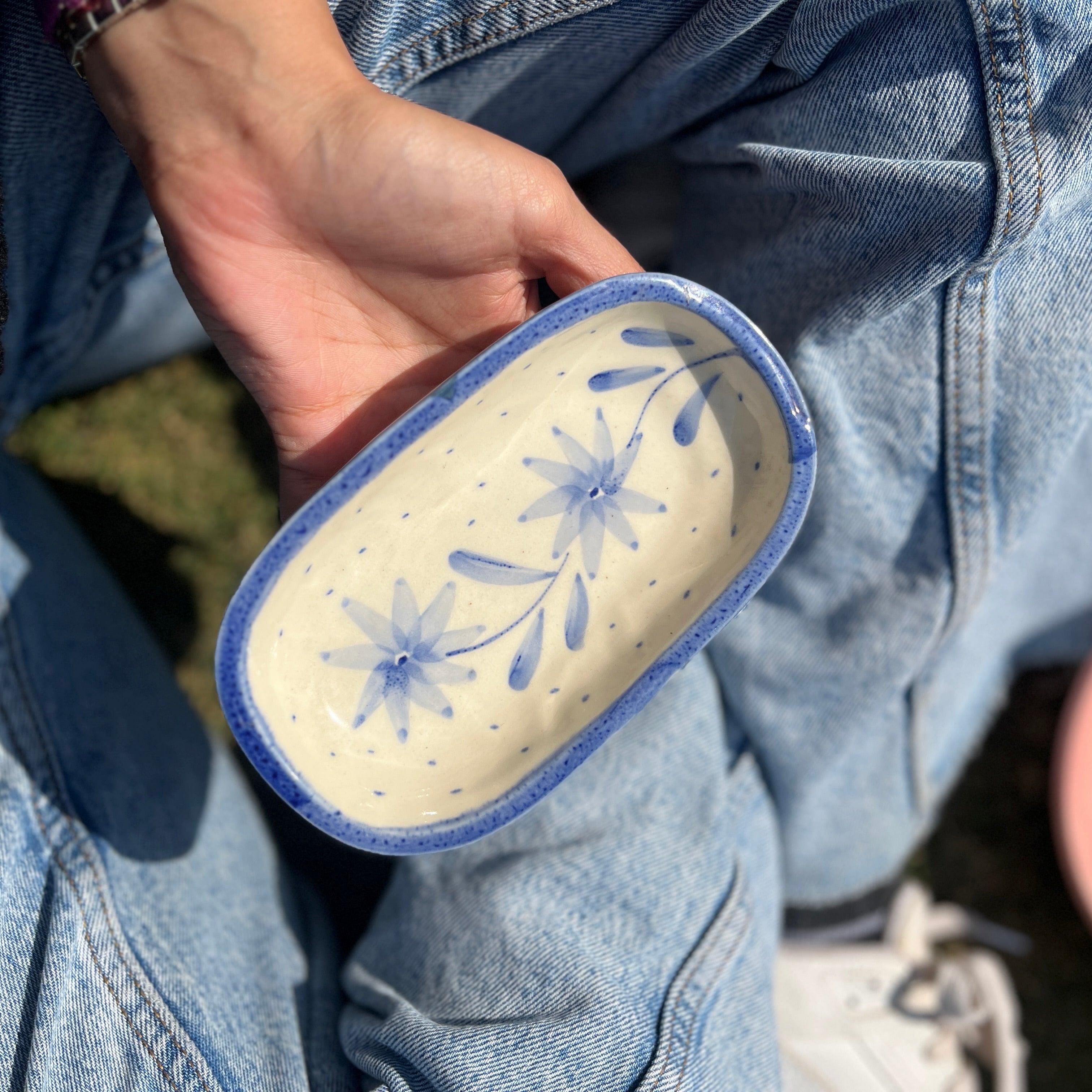 Hand holding a ceramic bowl with blue floral design against a blurred outdoor background