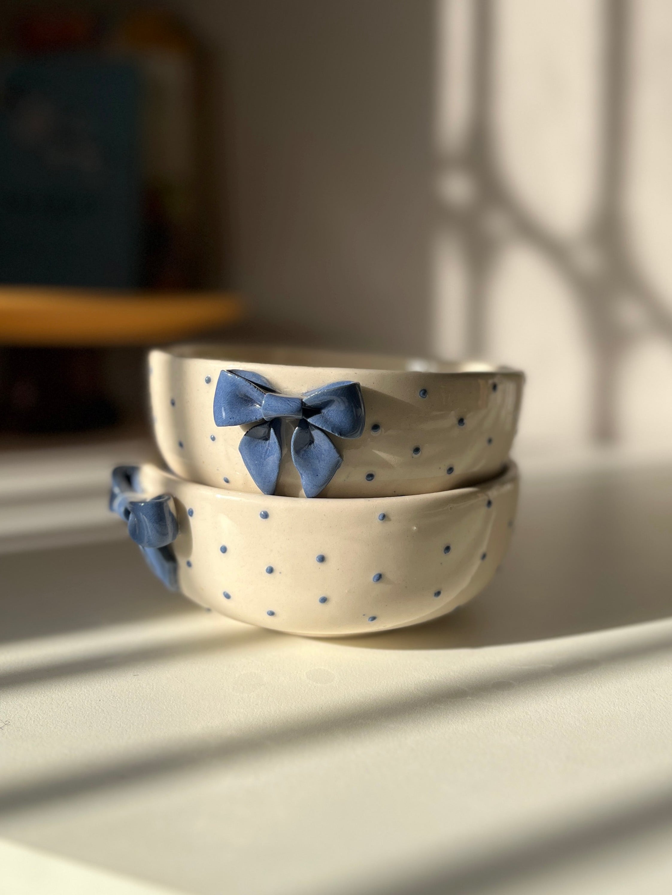 Two ceramic bowls with blue bow decorations on a light surface, with a blurred background.