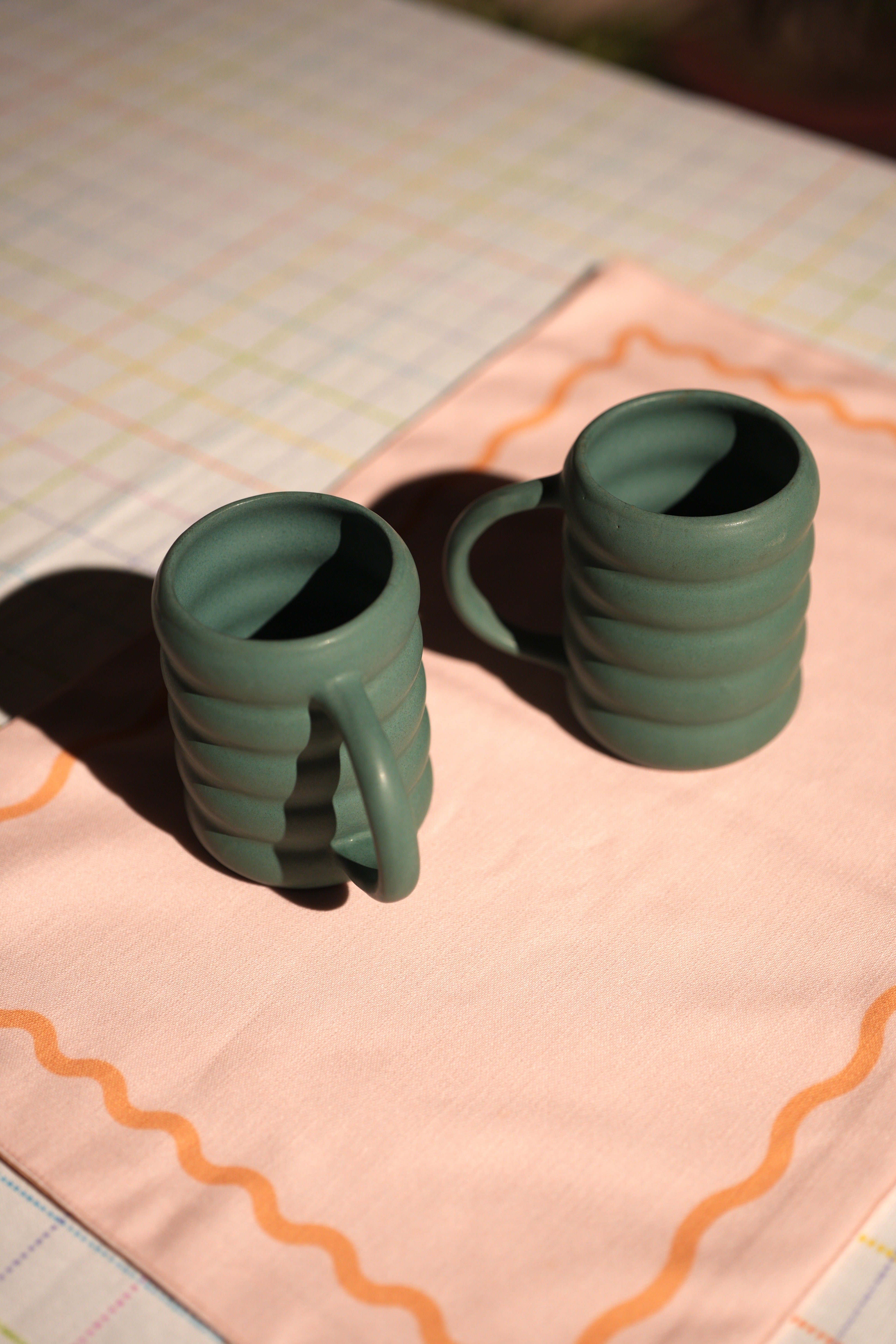 Two green ceramic mugs on a pink cloth with a grid background