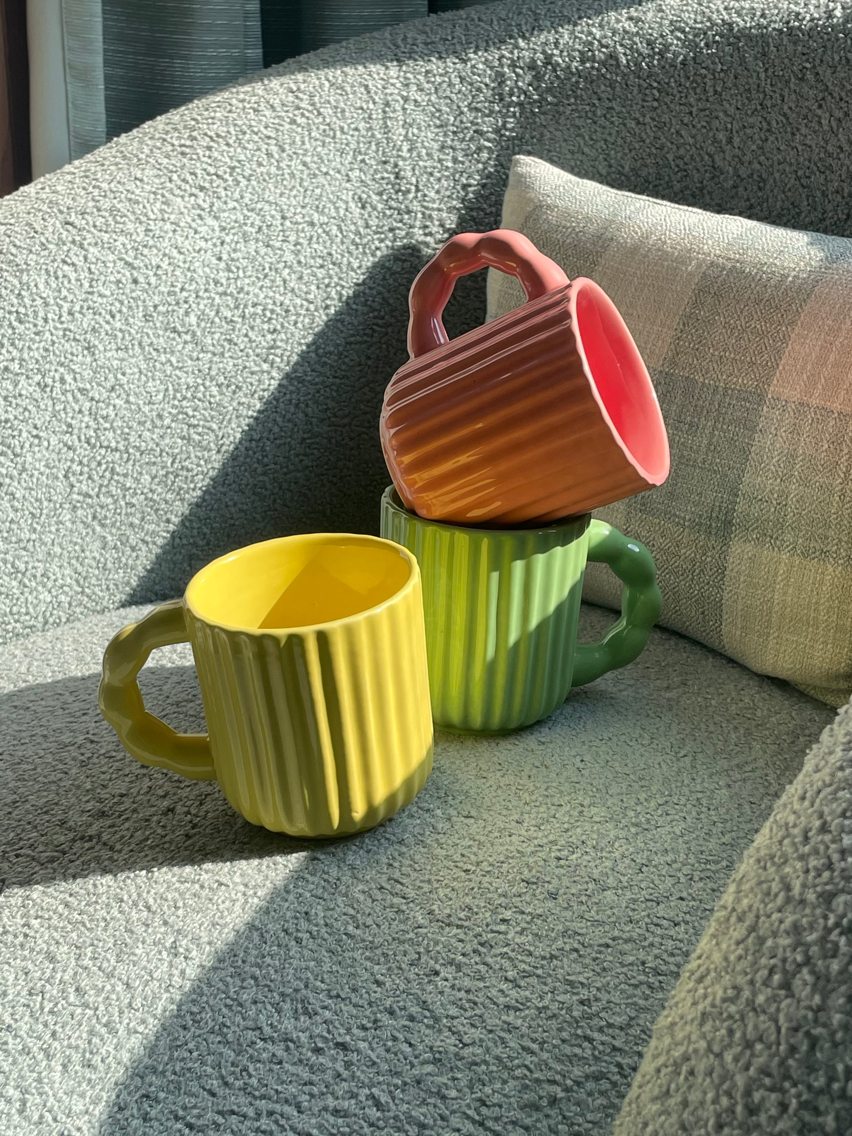 Three colourful fluted ceramic mugs styled together on a sofa chair