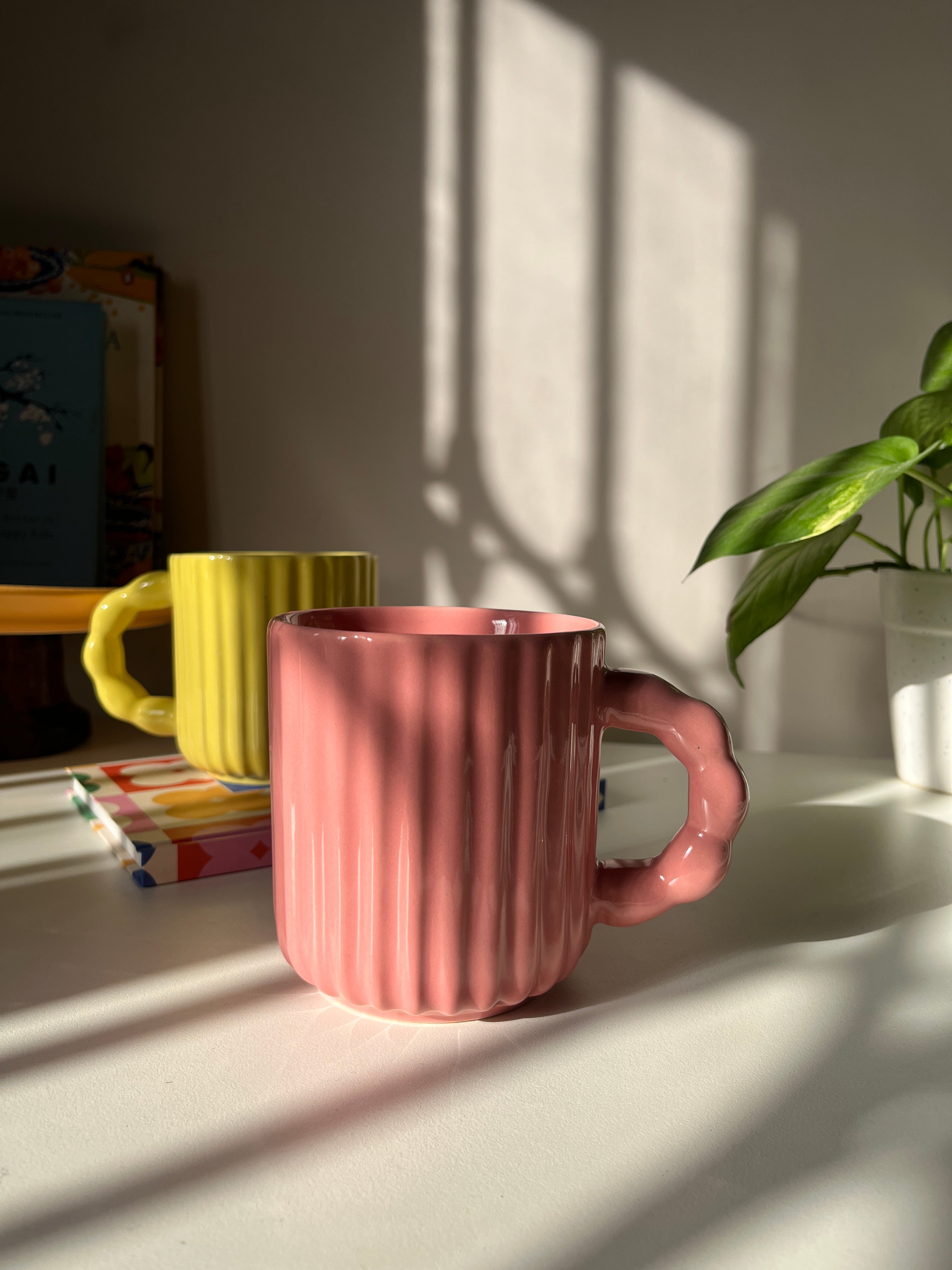 Pink ribbed mug on a white surface with shadows