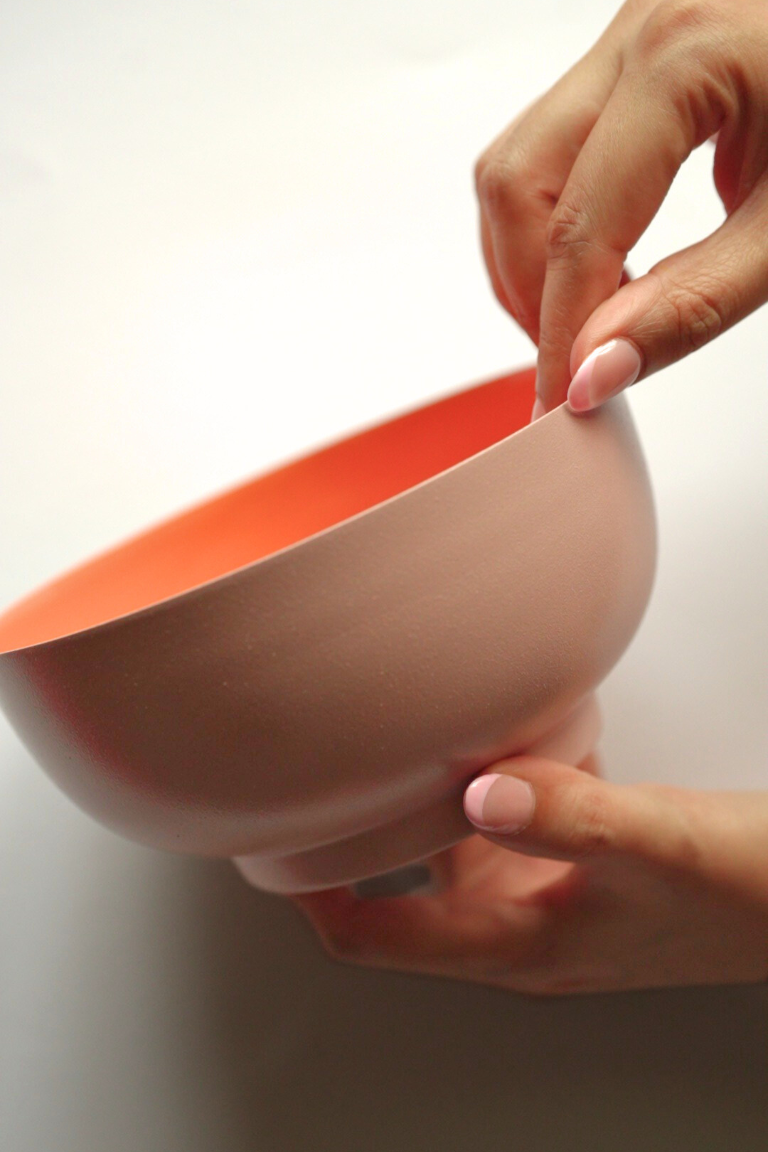 Person holding a pink and orange metal fruit salad bowl against a white background