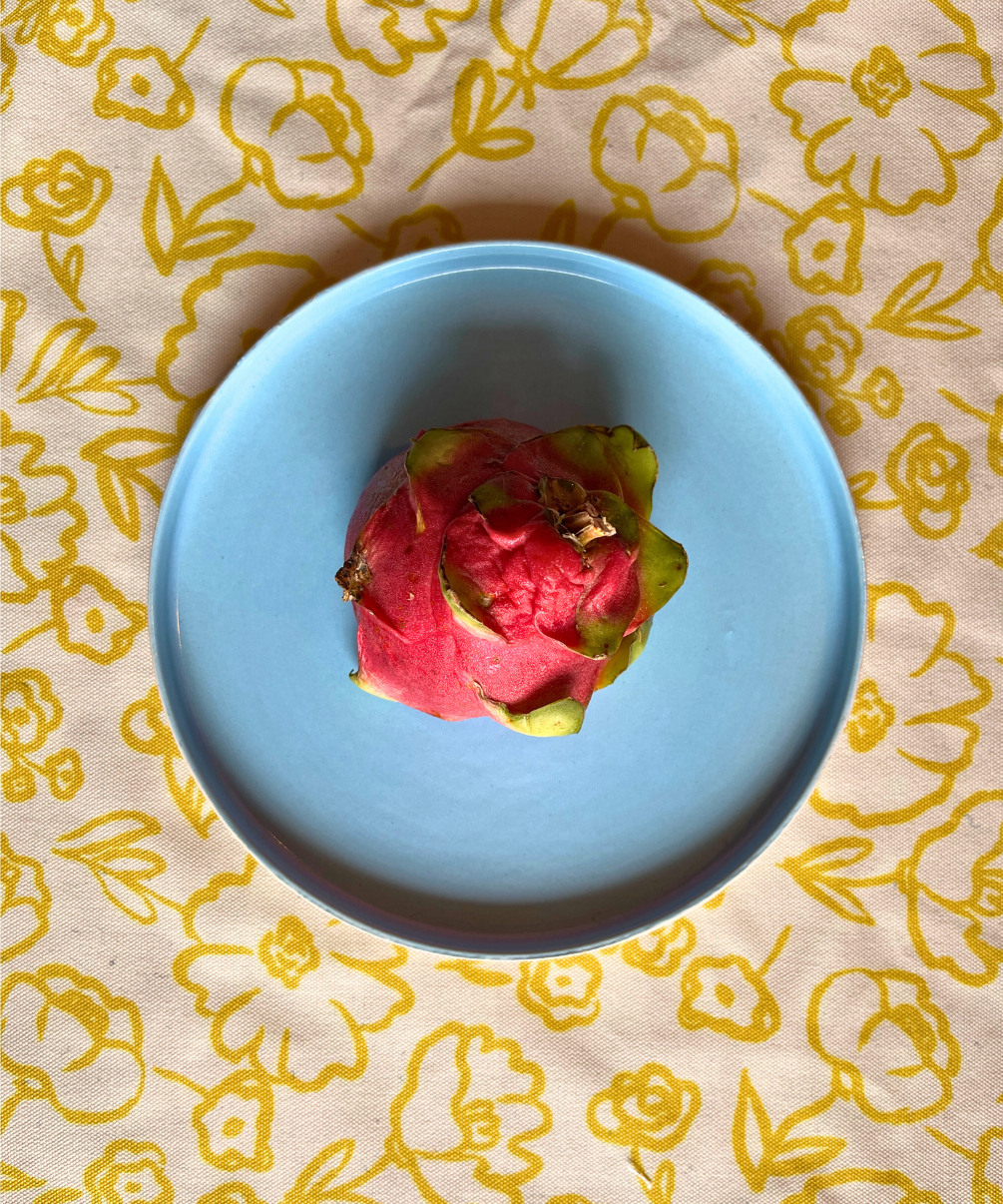 Cloud ceramic snack plate in pastel blue with a dragon fruit on a floral-patterned fabric background