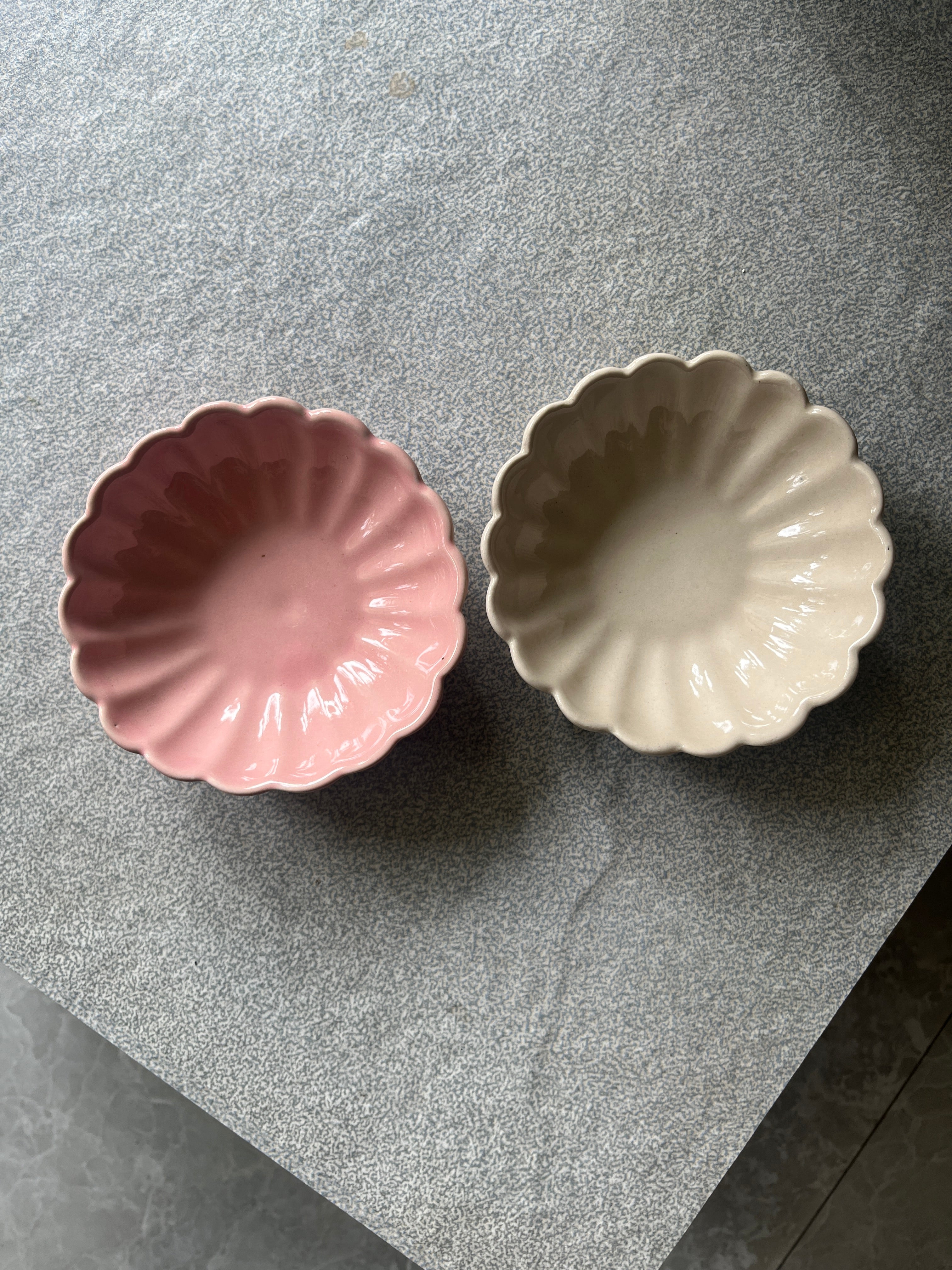 Two ceramic flower bowls, one white and one pink, on a gray surface.