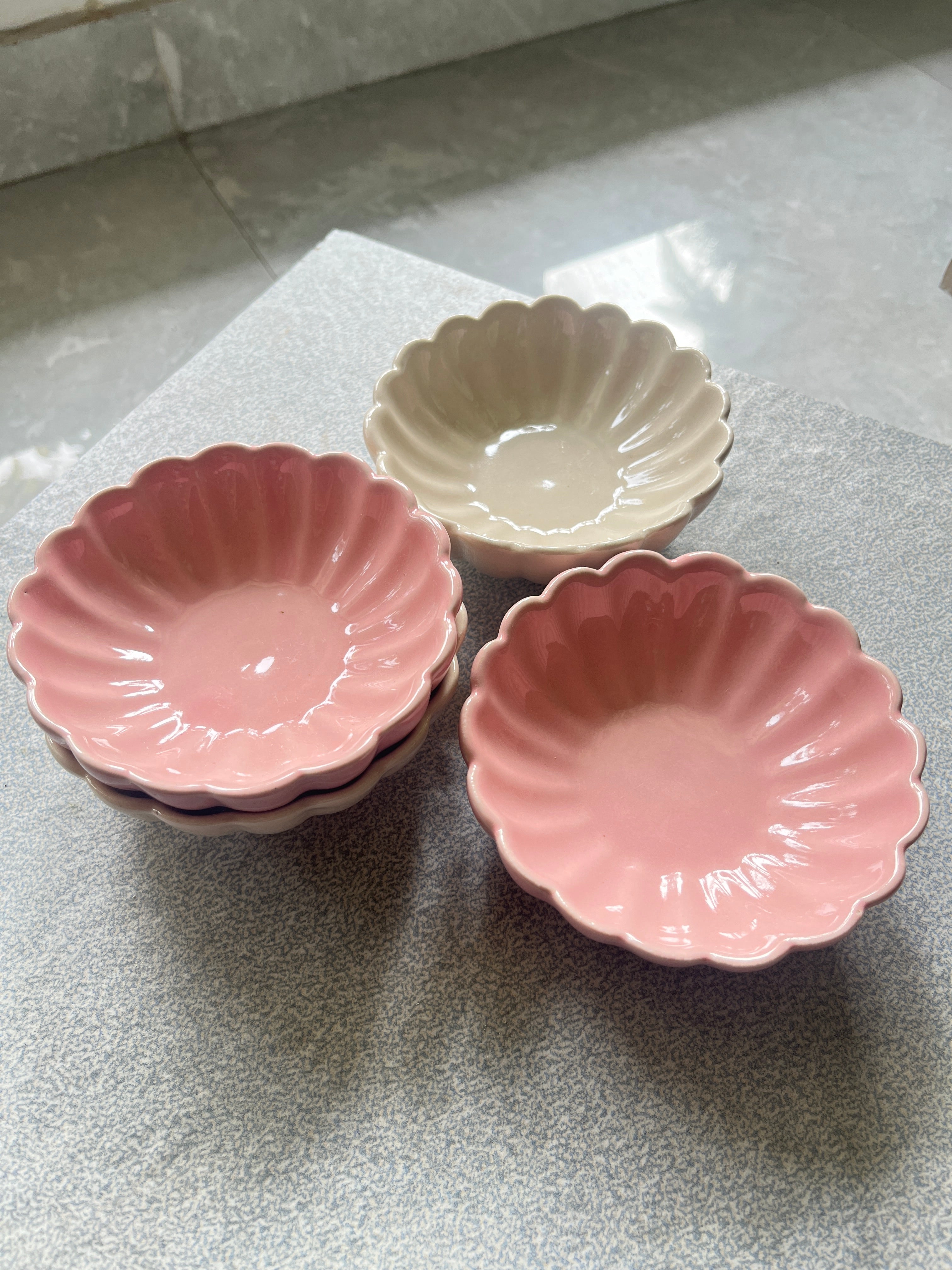 Multiple daisy flower ceramic bowls with scalloped edges in pink, and white on a marble surface.