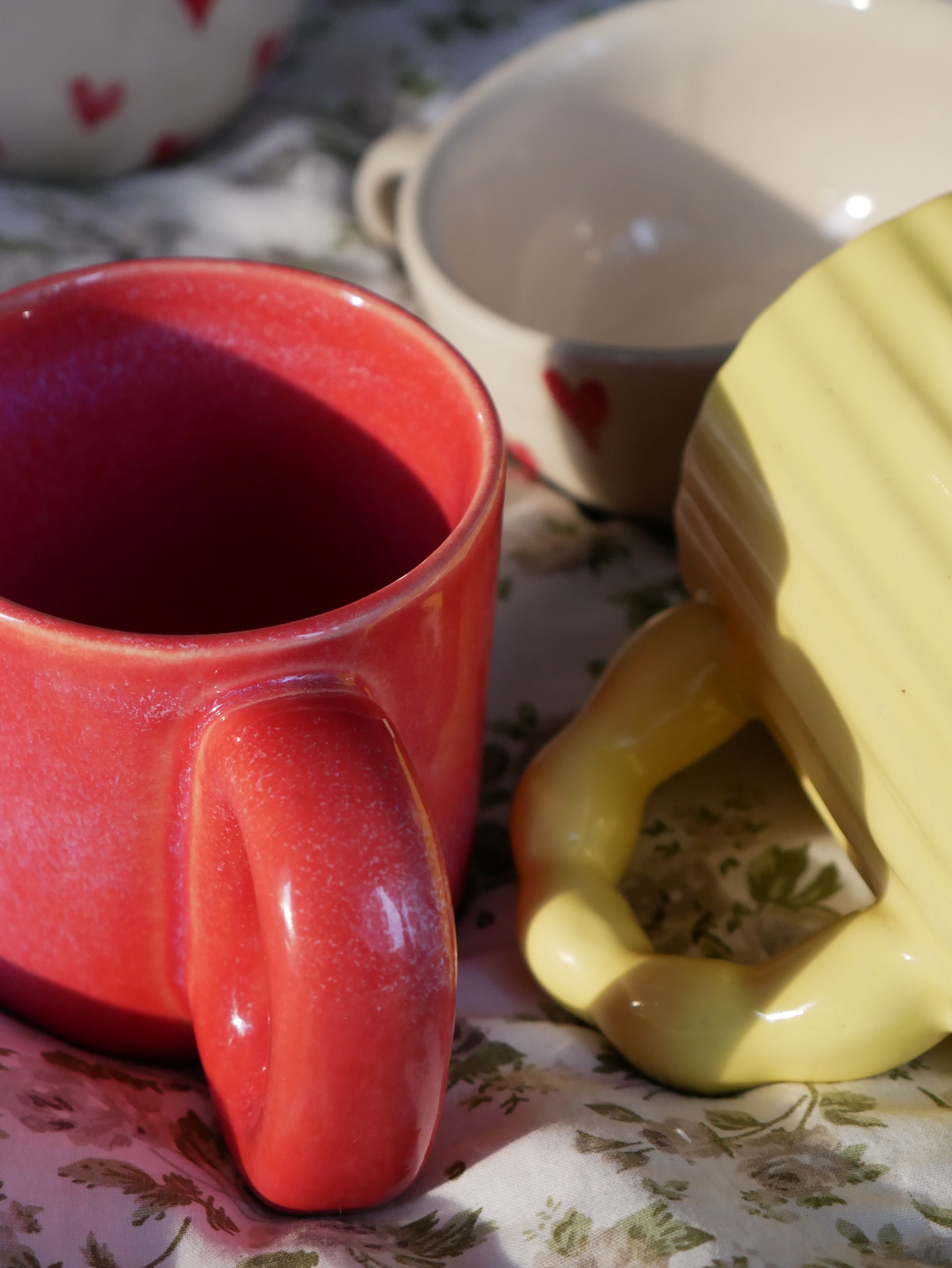 Red ember ceramic mug and yellow sunbeam madam jan mug on a floral-patterned surface