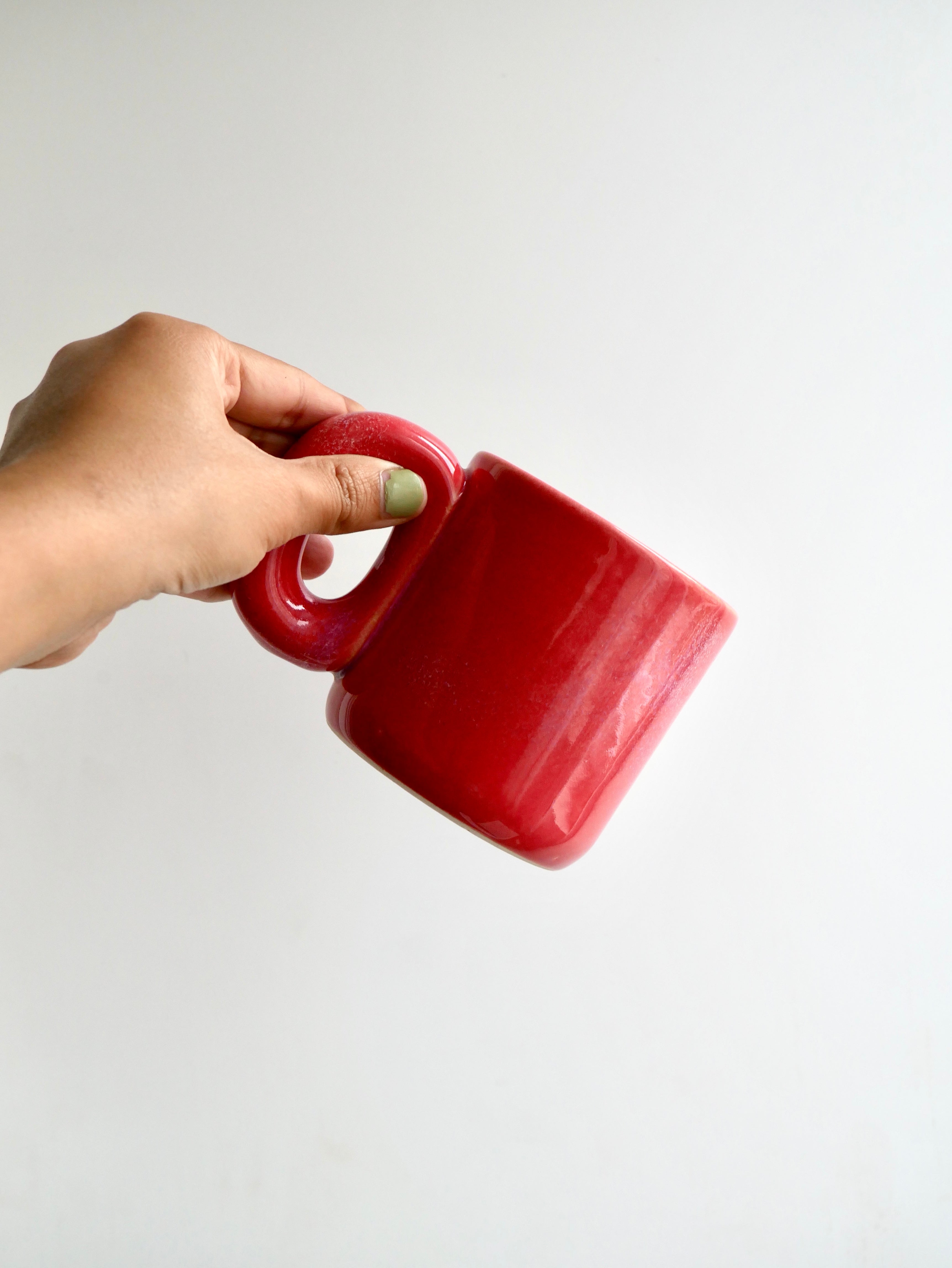 Hand holding a ceramic red glossy mug against a white background