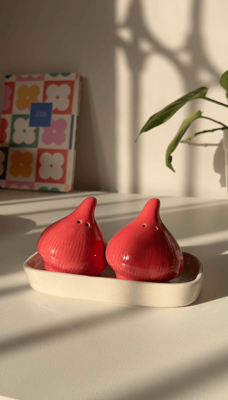 A pair of red onion shaped salt and pepper shakers set with a white ceramic tray. 