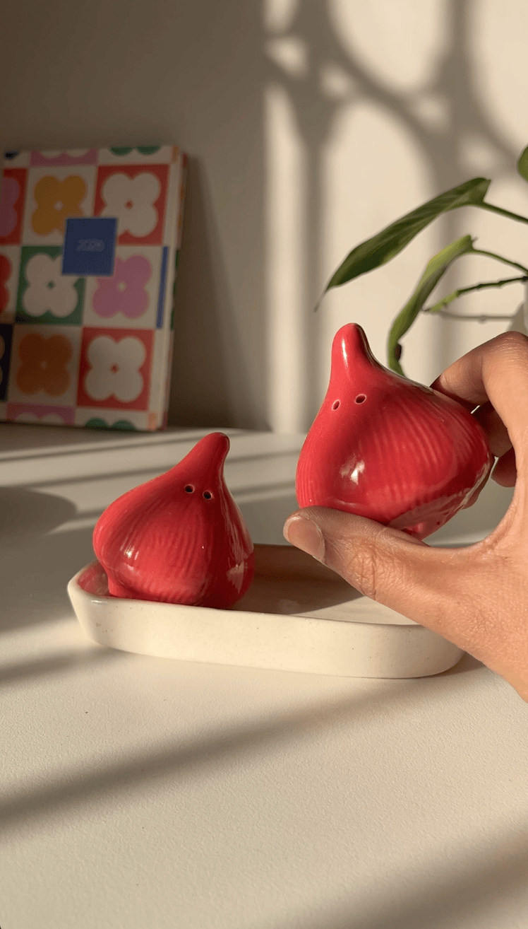 2 Red salt and pepper shakers in shape of onions with a red ceramic trinket tray along as a base.
