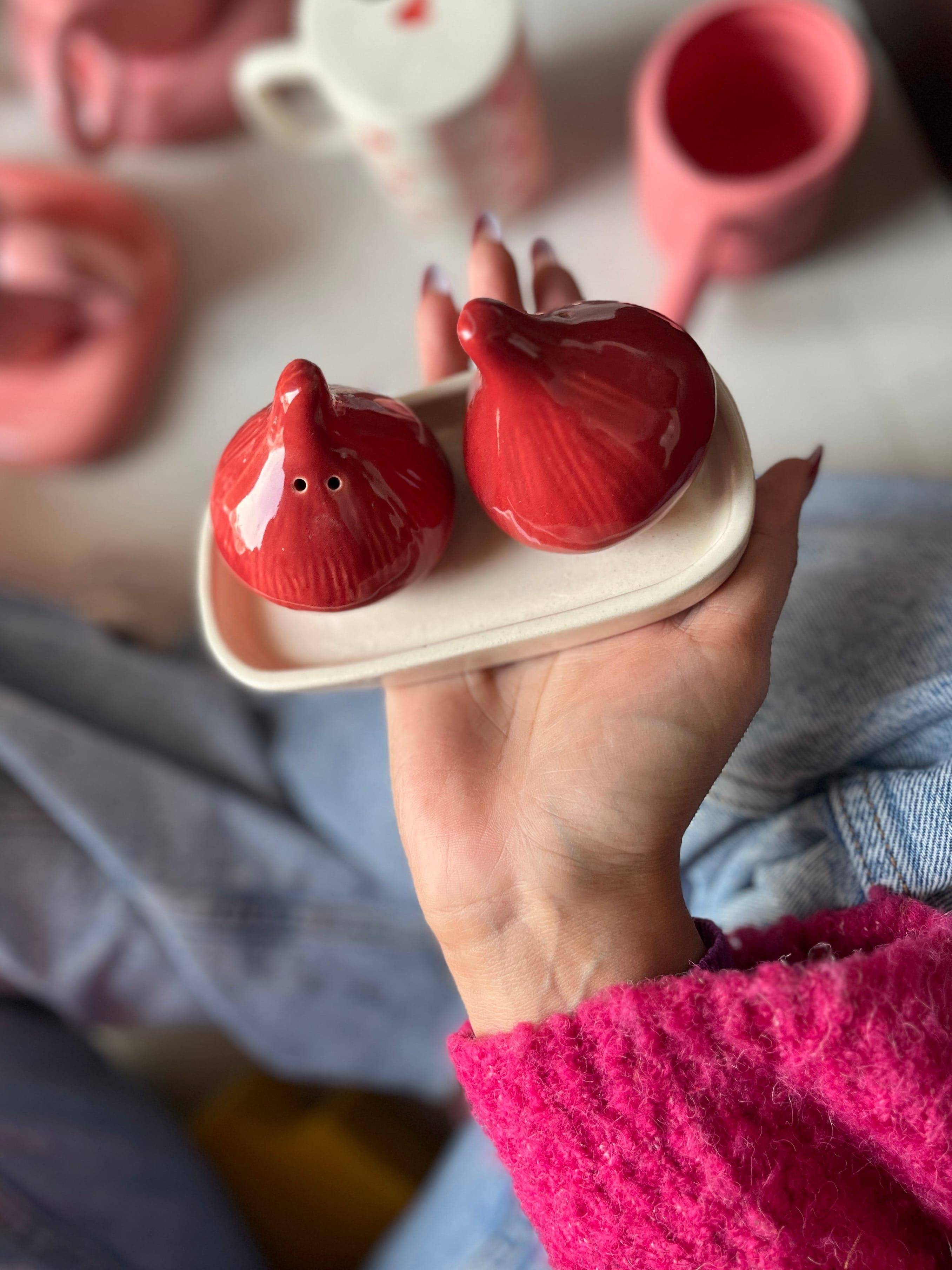 Hand holding a red ceramic onion-shaped salt and pepper shaker with a white base.