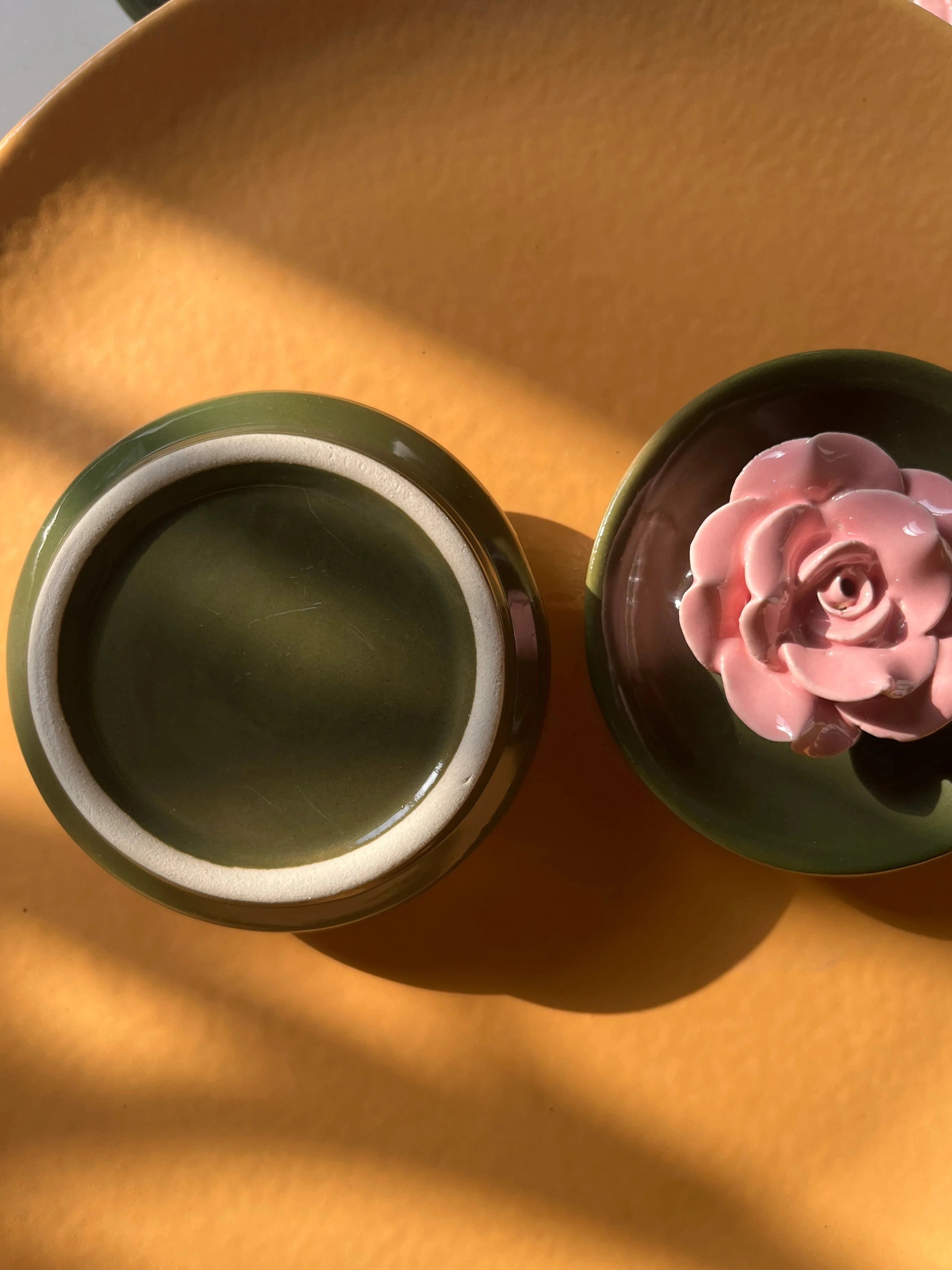 Royal green ceramic incense stick holder with pink flower detail front and back view on a yellow plate. 