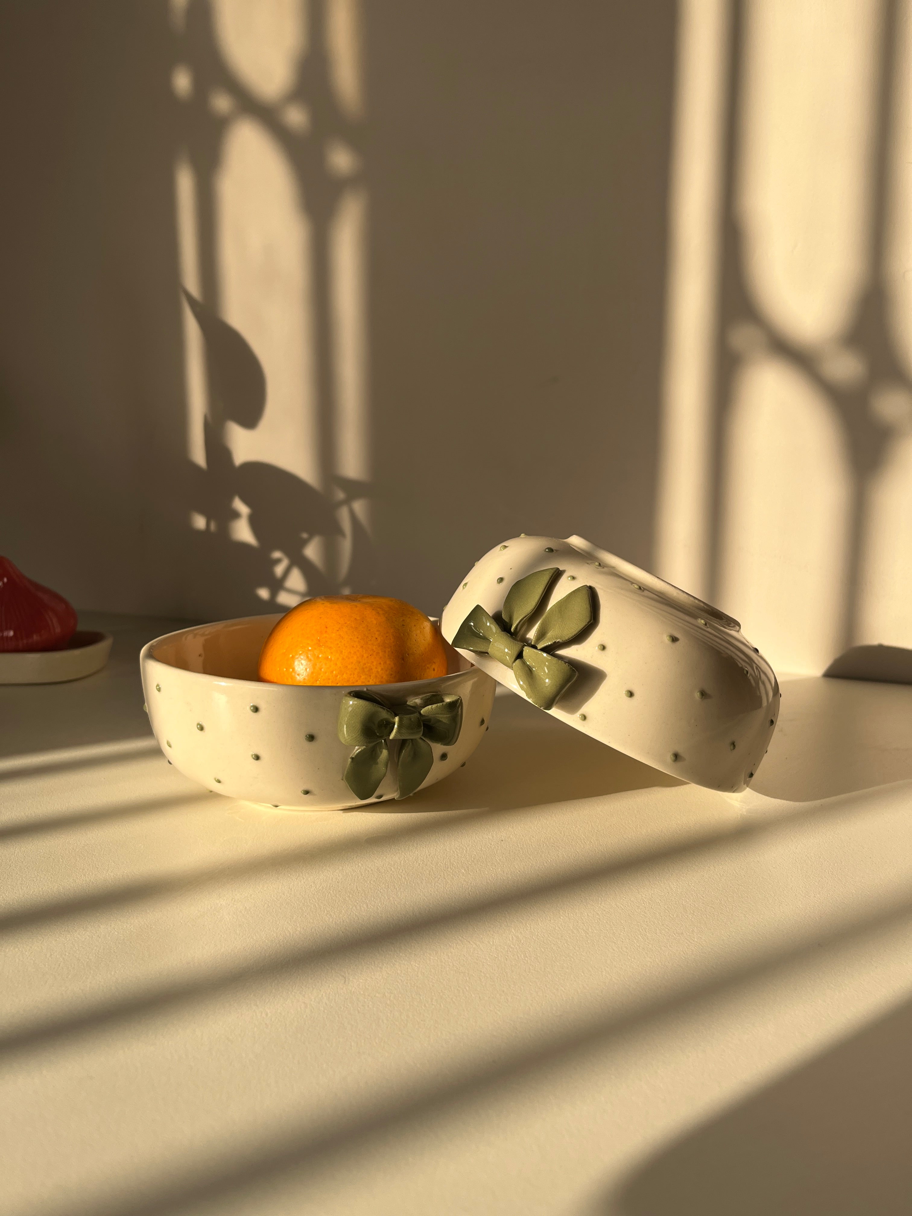 Styled shot of green ceramic bowl with sculptural ribbon bow accent with a fruit