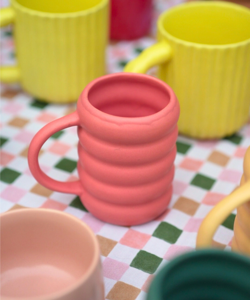 Pink matte bubble solid tone mug on a checkered tablecloth with yellow sunbeam and green buttercup in the background