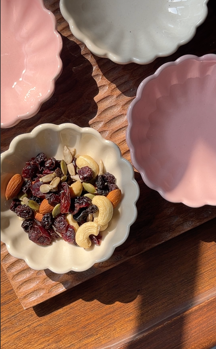 Small bowl of mixed nuts and dried fruits on a wooden surface with other bowls around.