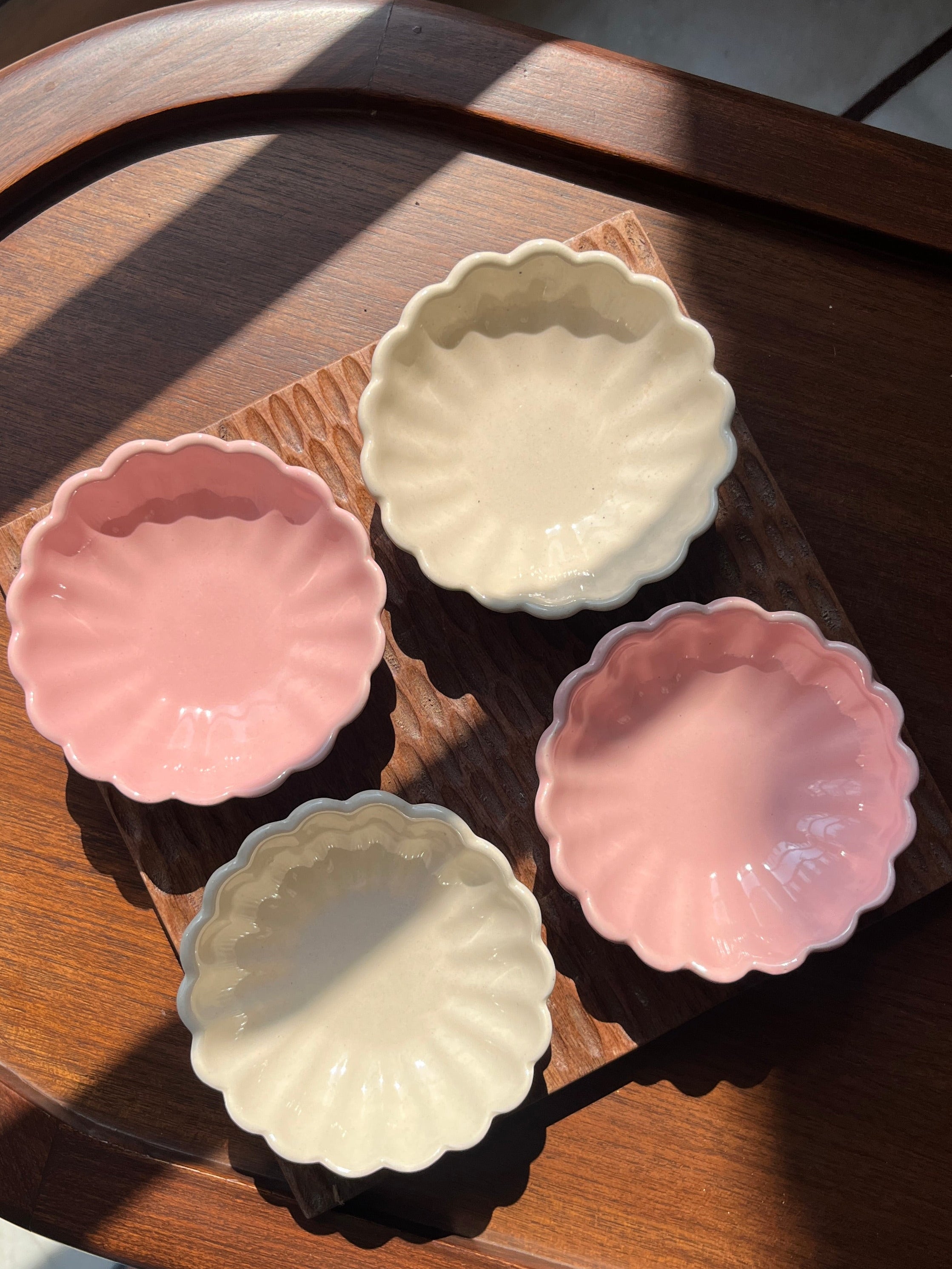 Four small ceramic dishes in pastel colors on a wooden scalloped tray. 