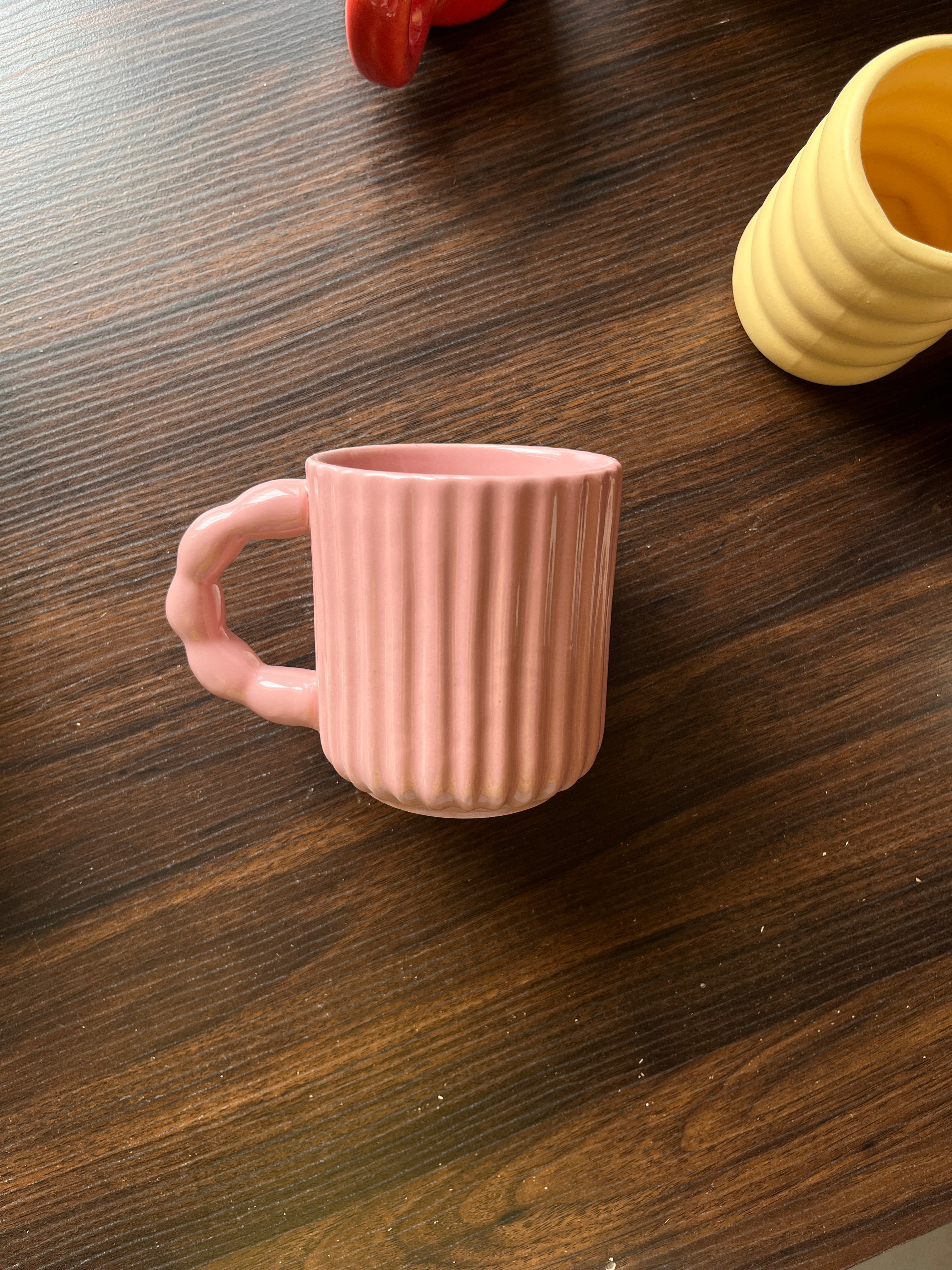 Side view of pink mug with ribbed texture on a wooden surface