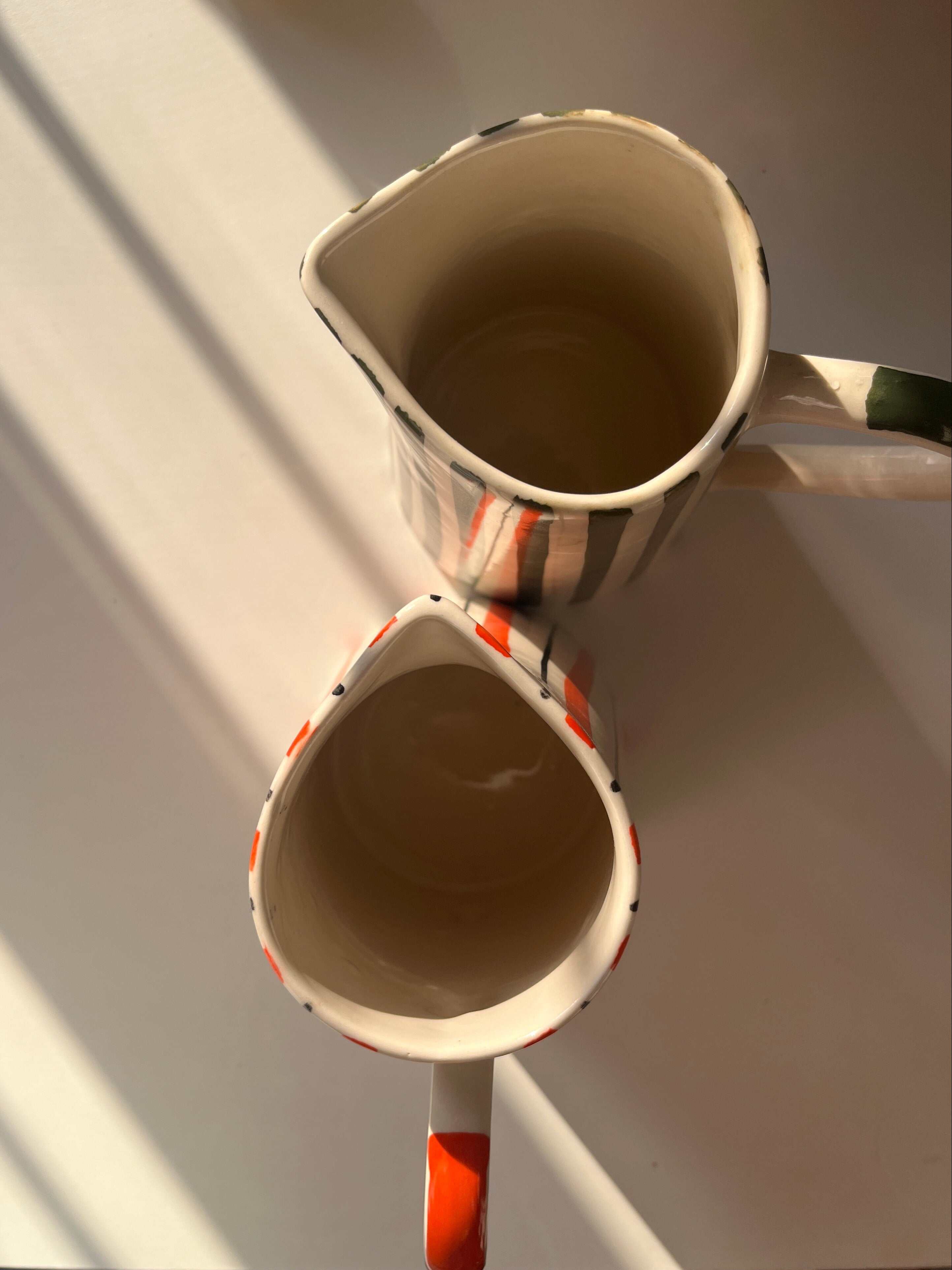 top view of hand-painted ceramic jug with orange stripes and curved handle along with basil jug