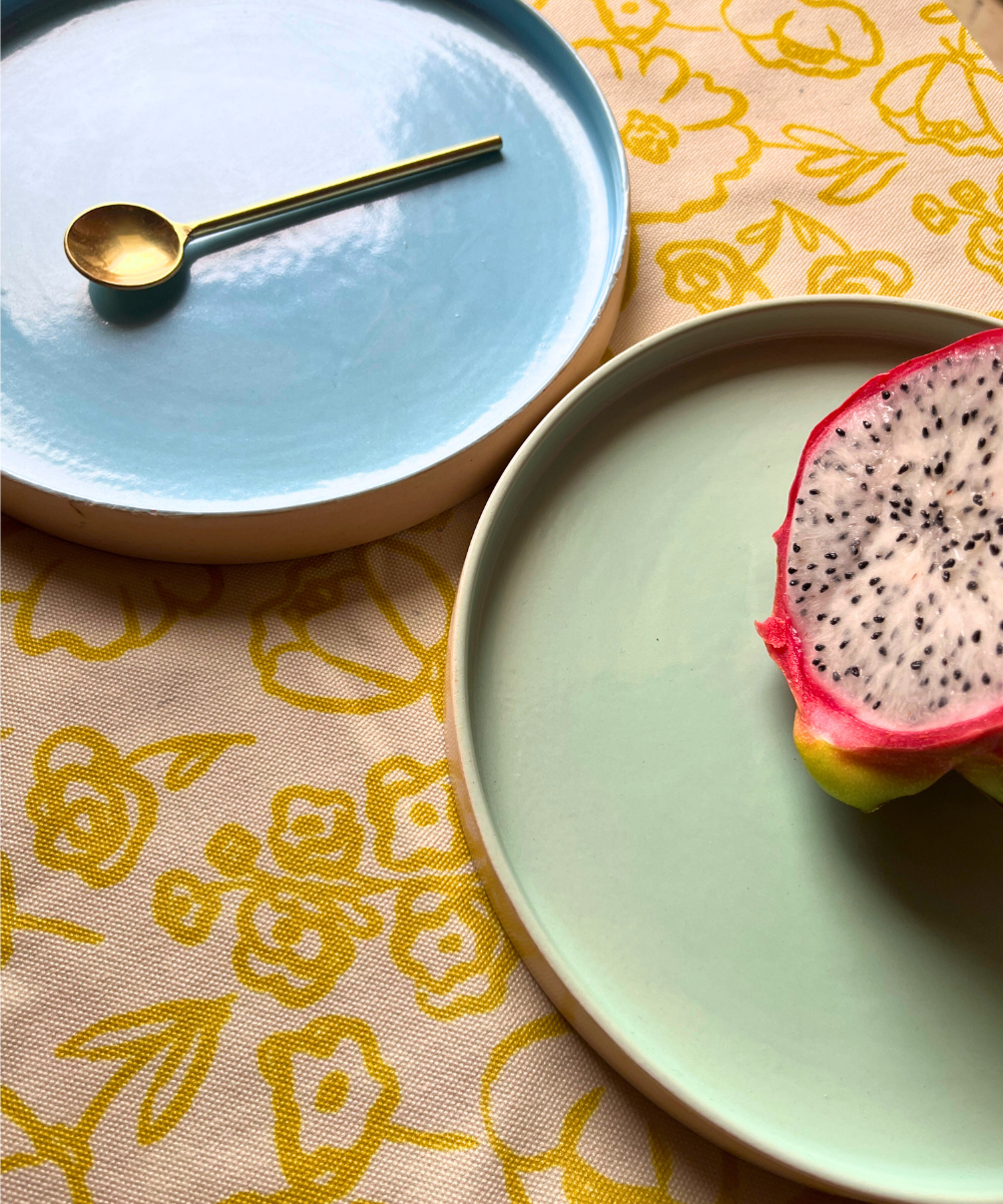 Two blue and green ceramic plates with a half-eaten dragon fruit and a gold spoon on a floral tablecloth.