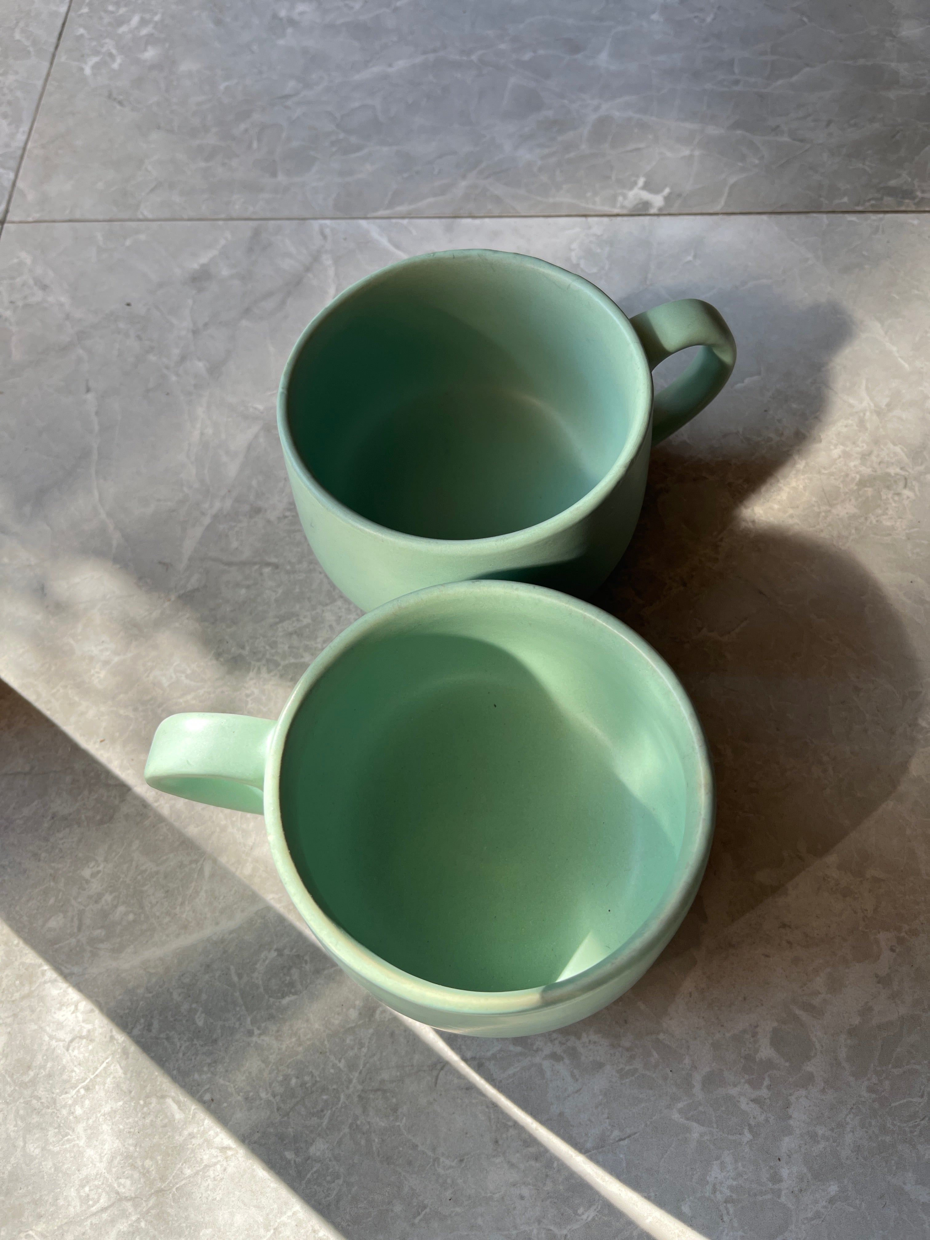 Top-shot of two minimal green ceramic cups with smooth matte texture