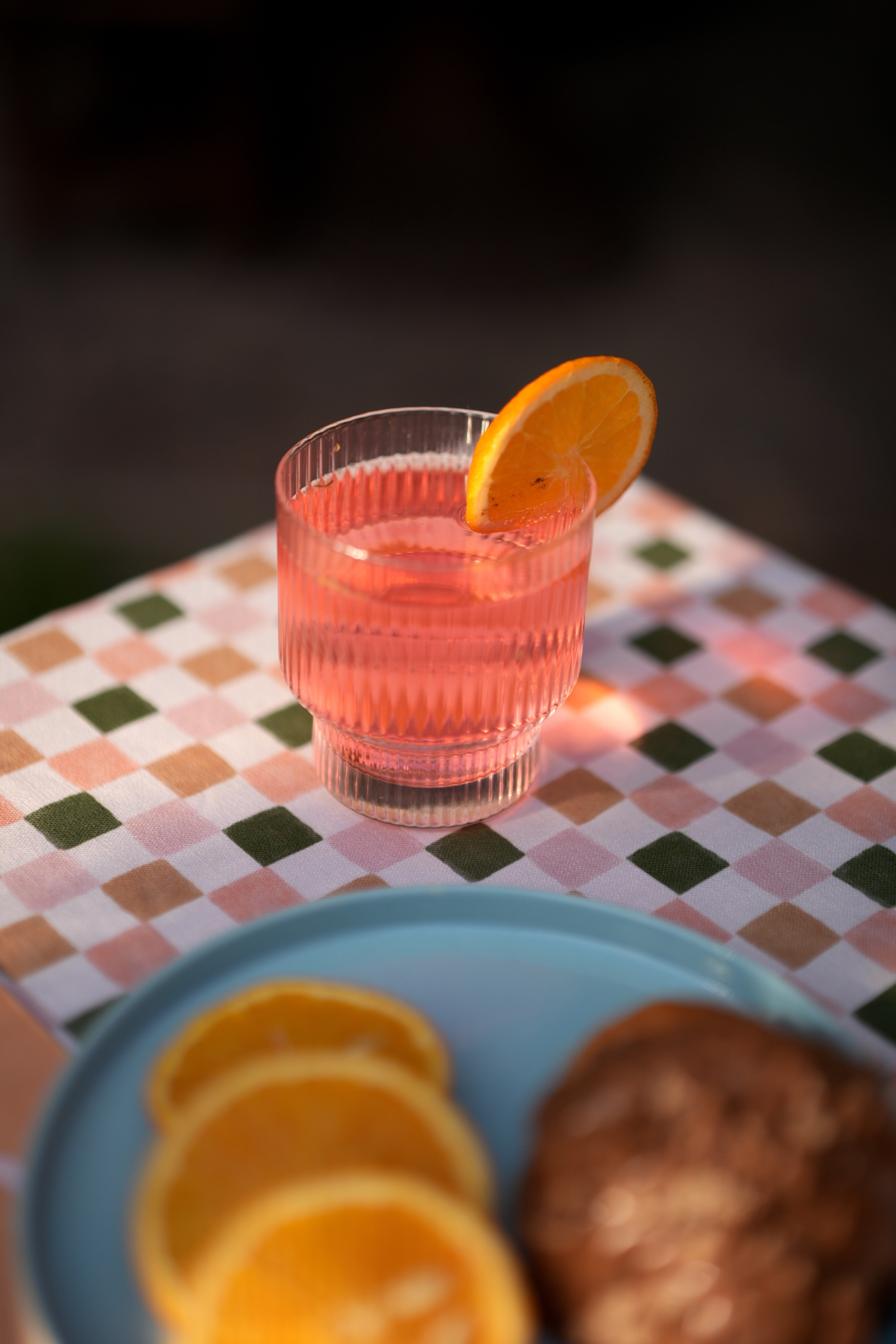 Pink cocktail with an orange slice in a fluted lucid glass on a checkered tablecloth