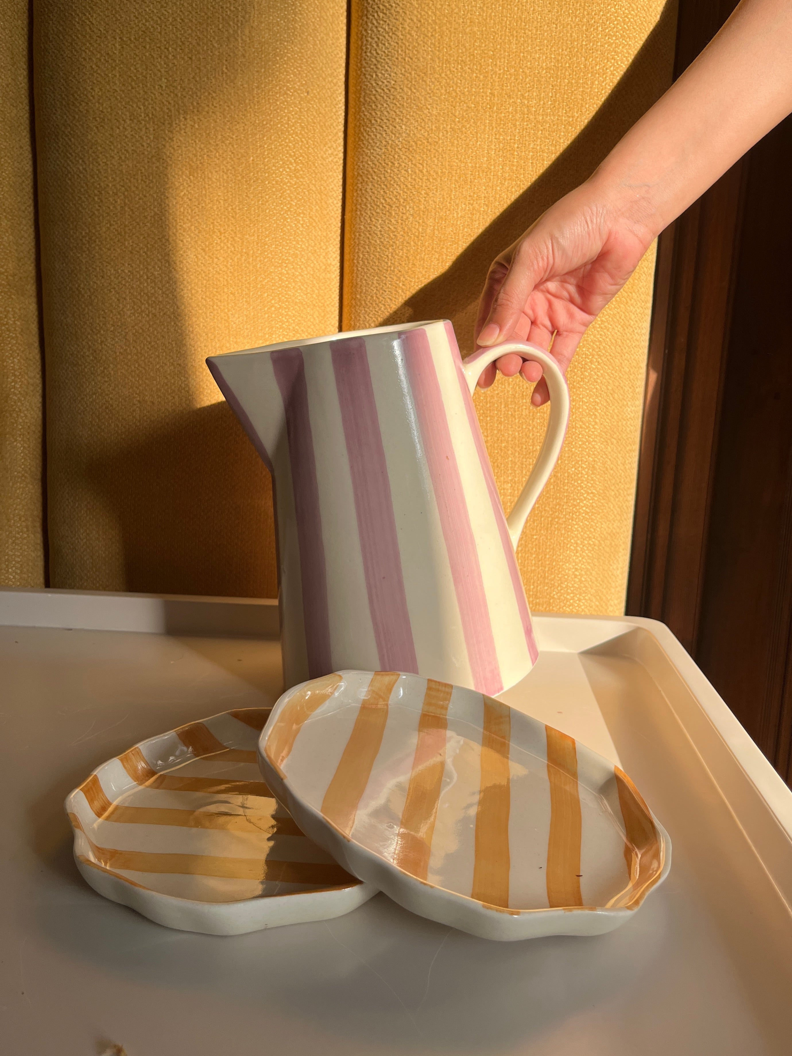 Person holding a striped mug next to matching striped slippers on a yellow background..