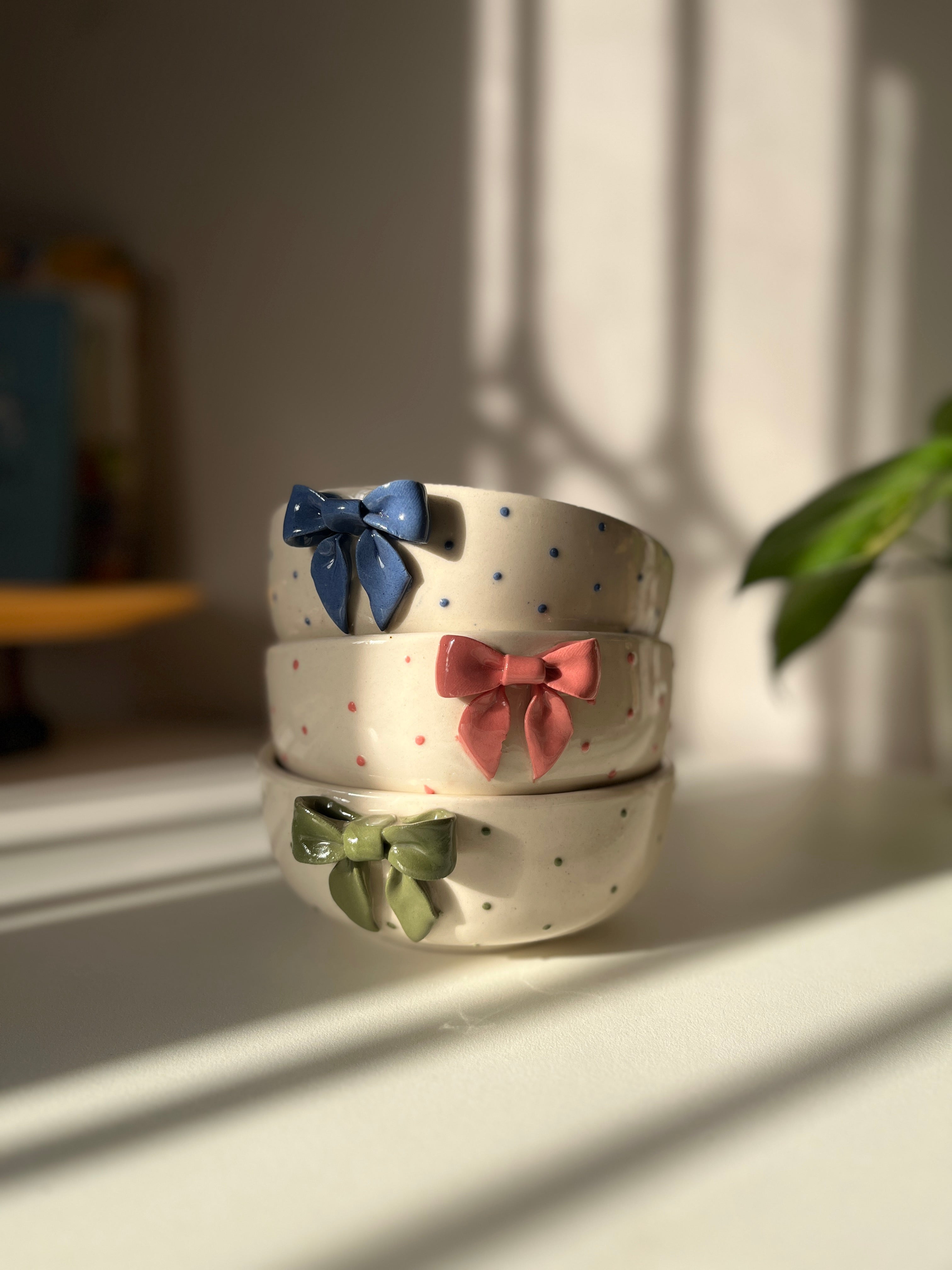 Three ceramic bowls with colorful bow decorations on a light surface.