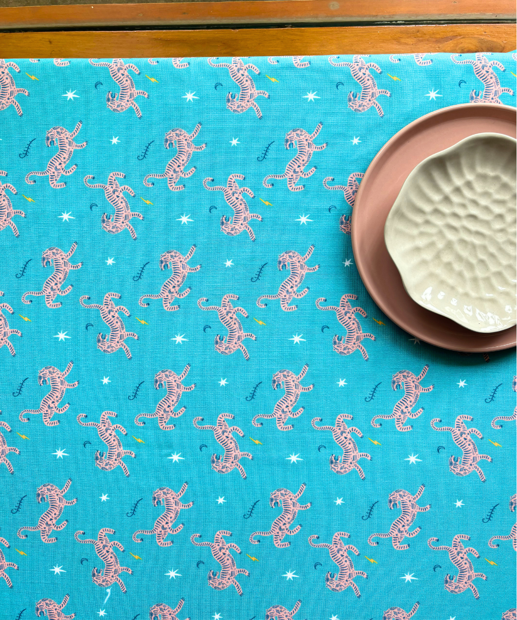 Blue fabric with pink tiger pattern, placed on a wooden surface with a ceramic dishes on top as decor