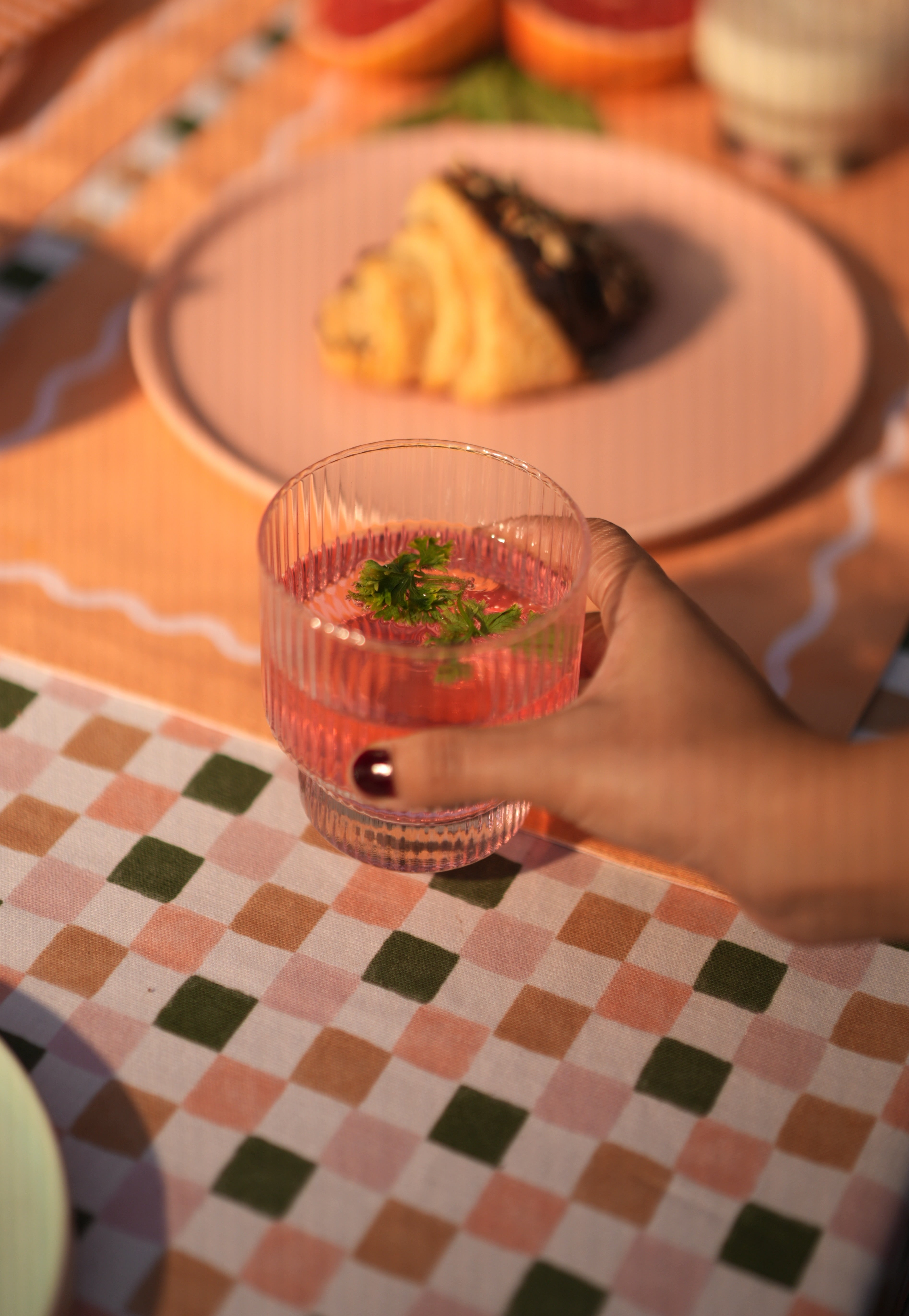 Hand holding a modern fluted glass with a drink on a checkered tablecloth