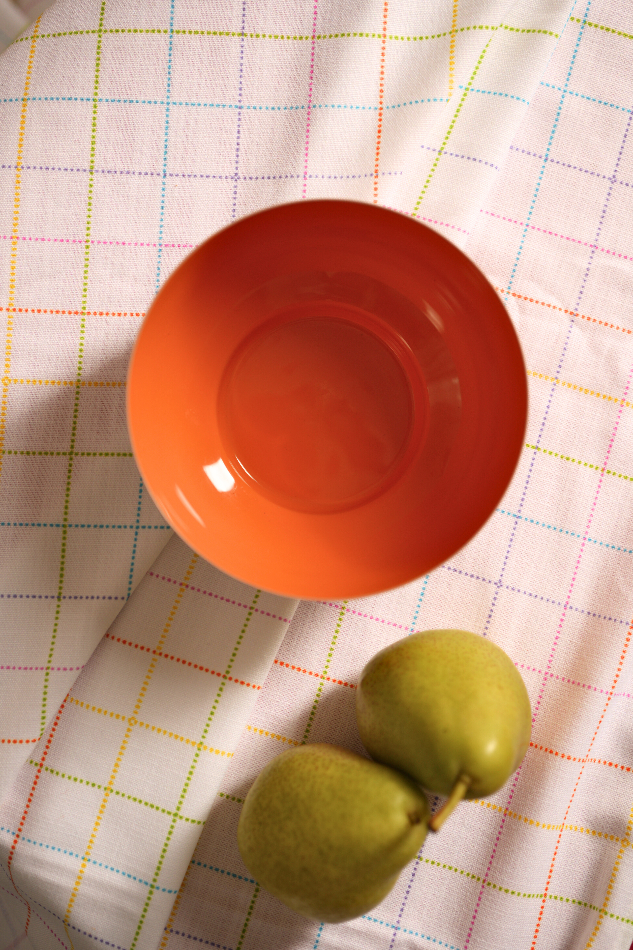 Orange metal bowl and green fruit on a checkered tablecloth