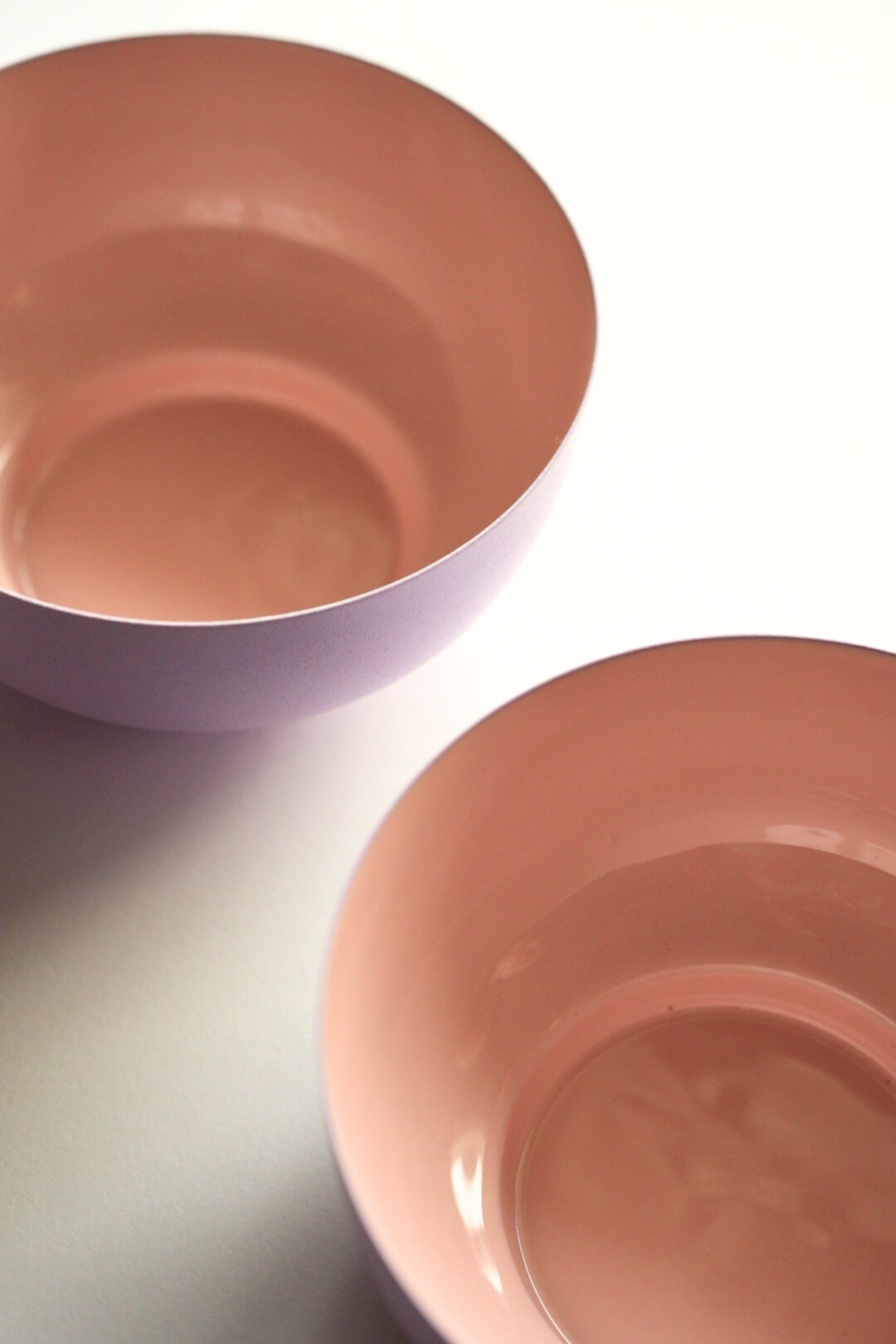 Two pink metal fruit bowls on a light gray surface