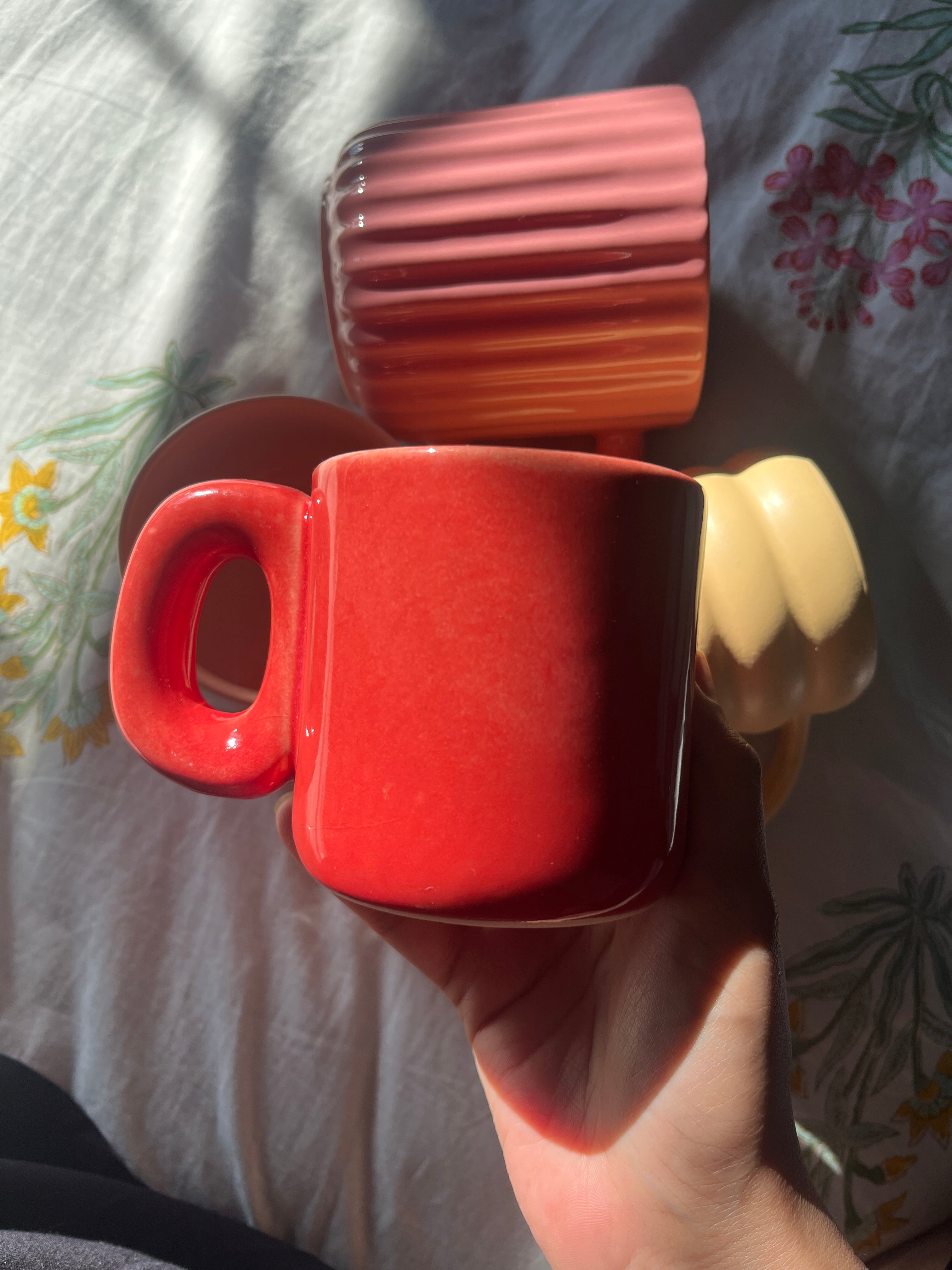 Red ember madam jan ceramic cup with a burnt look held by a hand on a patterned fabric background